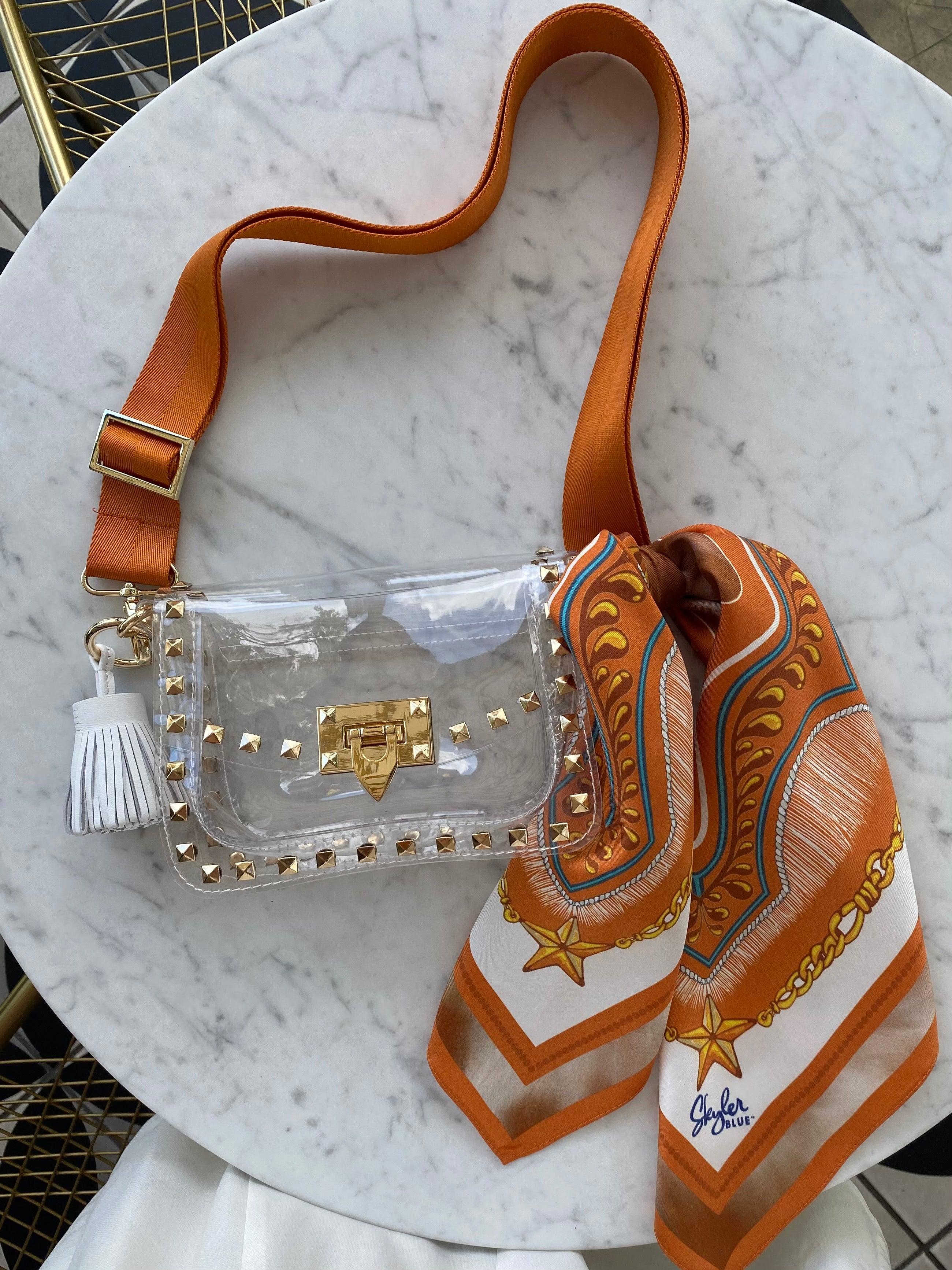 Skyler Blue’s The Austin 001 Small Studded Clear Bag stadium approved clear bag / clear purse including adjustable, nylon webbing shoulder or crossbody strap with herringbone weave and gold hardware, 60-centimeter 100% silk twill scarf, and 100% genuine leather tassel.