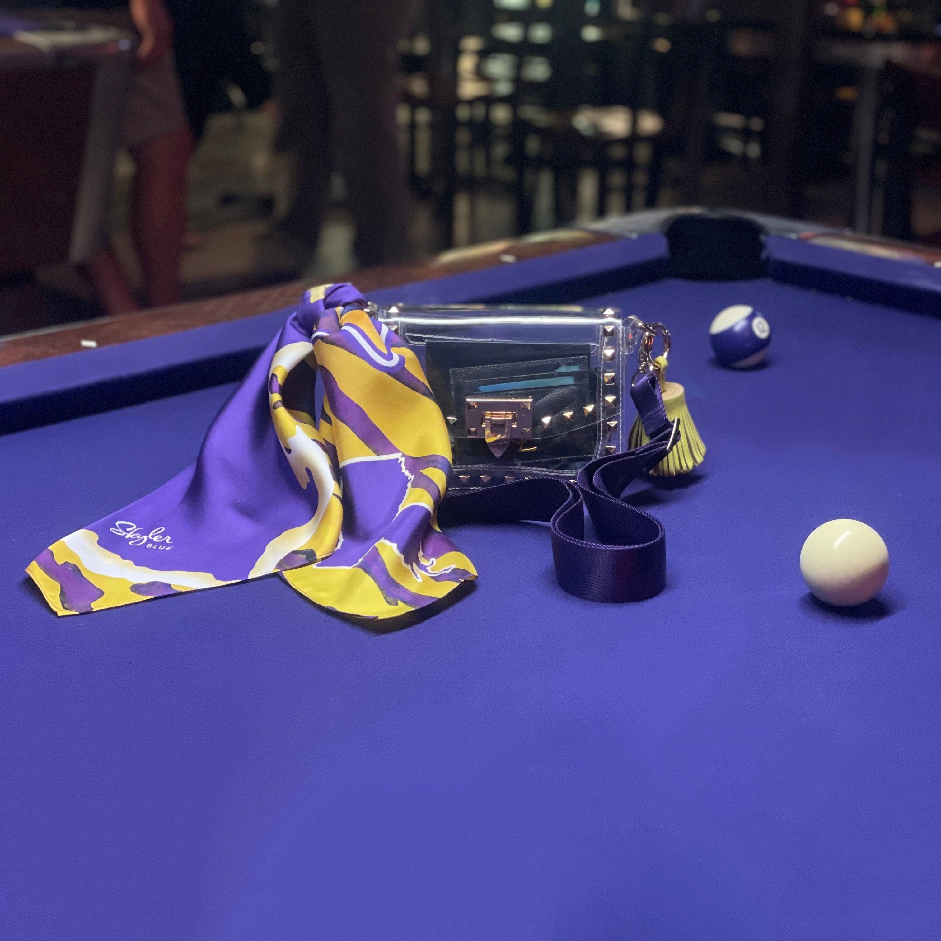 Skyler Blue’s The Baton Rouge Small Studded Clear Bag stadium approved clear bag / clear purse including adjustable, nylon webbing shoulder or crossbody strap with herringbone weave and gold hardware, 60-centimeter 100% silk twill scarf, and 100% genuine leather tassel.