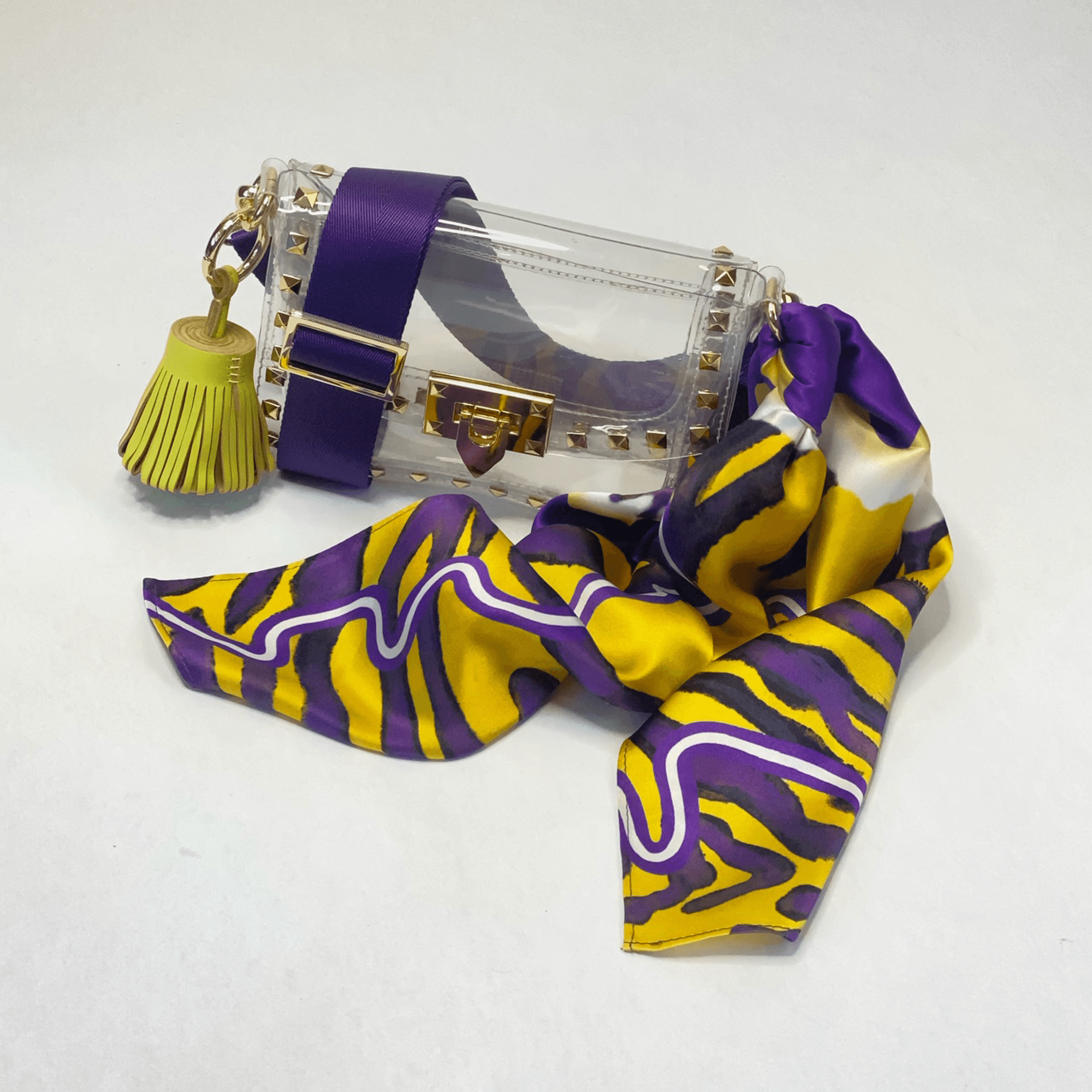 Skyler Blue’s The Baton Rouge Small Studded Clear Bag stadium approved clear bag / clear purse including adjustable, nylon webbing shoulder or crossbody strap with herringbone weave and gold hardware, 60-centimeter 100% silk twill scarf, and 100% genuine leather tassel.