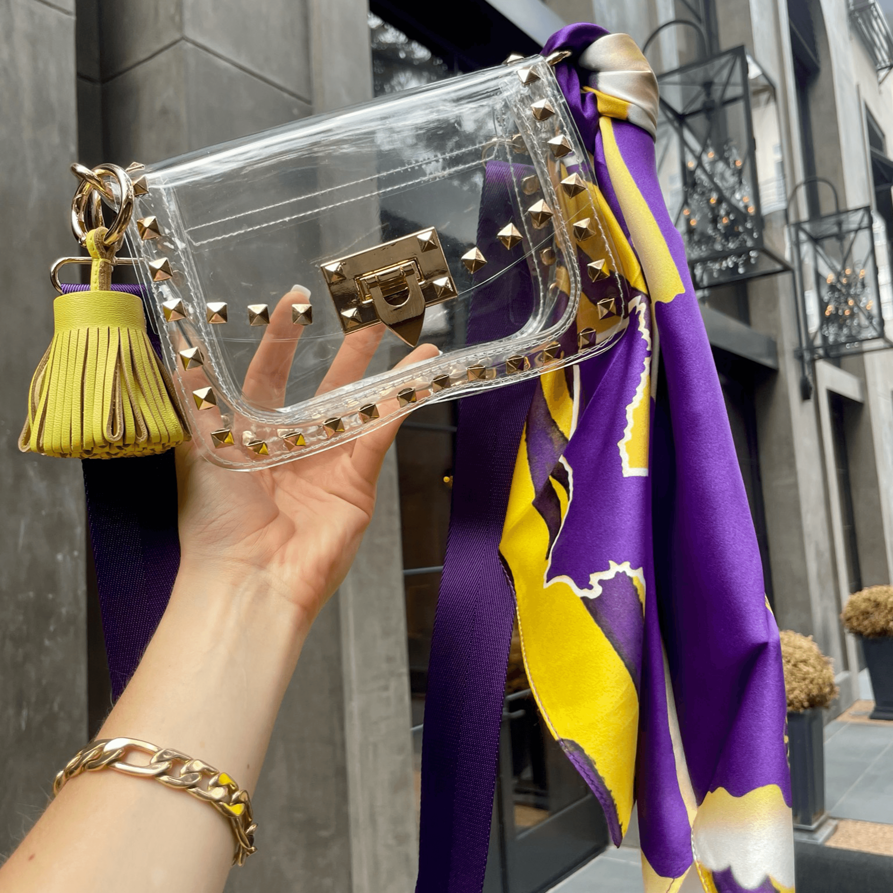 Skyler Blue’s The Baton Rouge Small Studded Clear Bag stadium approved clear bag / clear purse including adjustable, nylon webbing shoulder or crossbody strap with herringbone weave and gold hardware, 60-centimeter 100% silk twill scarf, and 100% genuine leather tassel.