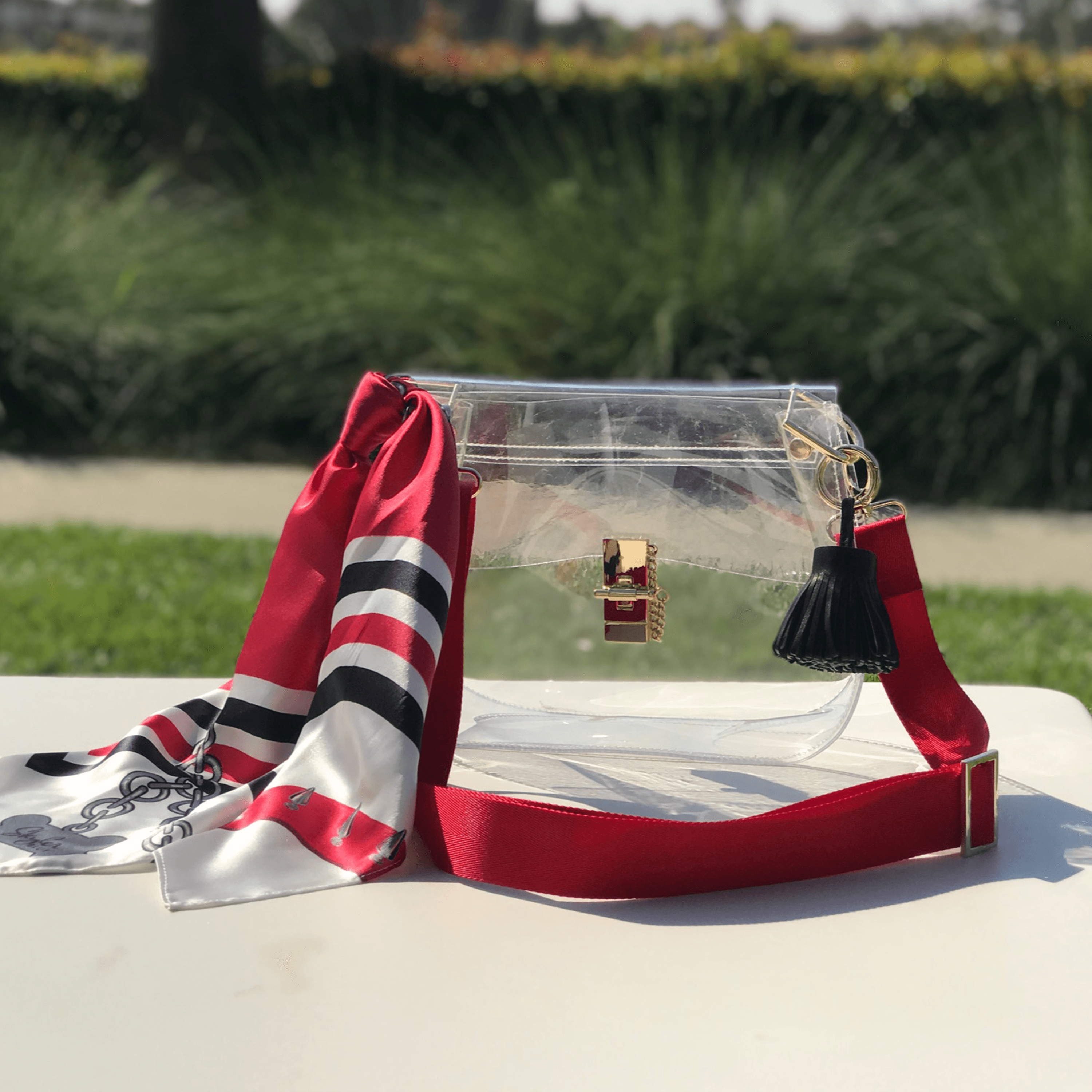 Skyler Blue’s The Athens 001 Medium Saddle Clear Bag stadium approved clear bag / clear purse including adjustable, nylon webbing shoulder or crossbody strap with herringbone weave and gold hardware, 60-centimeter 100% silk twill scarf, and 100% genuine leather tassel.