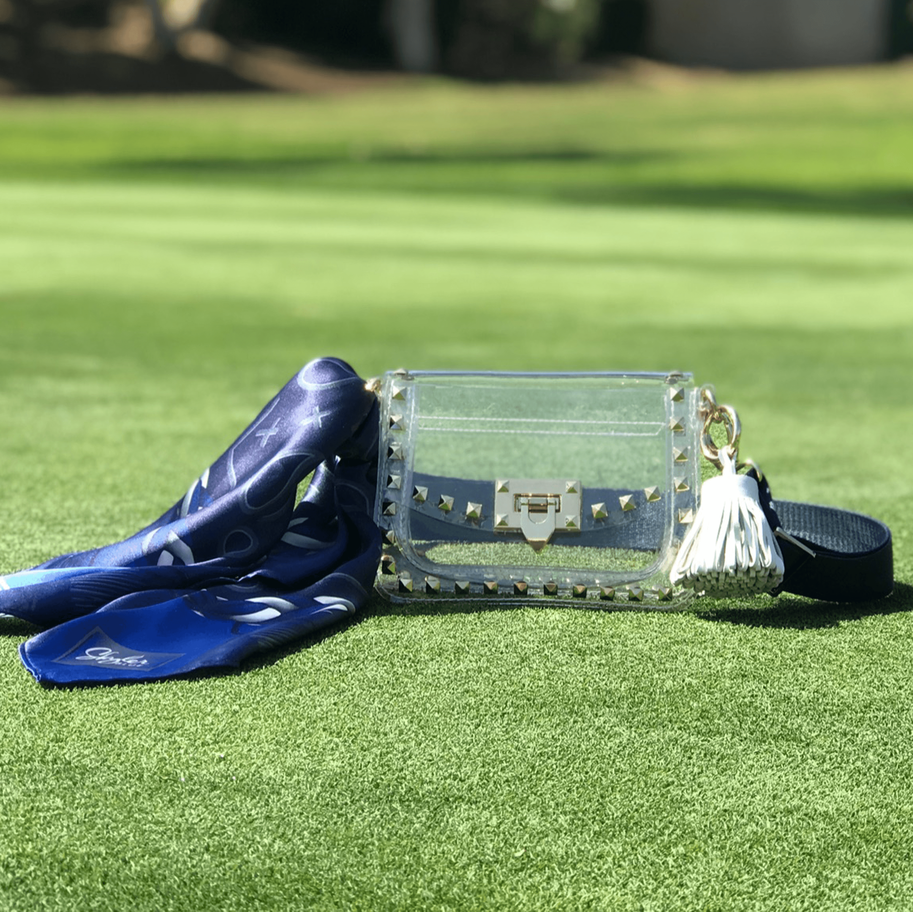 Skyler Blue’s The Dallas 001 Small Studded Clear Bag stadium approved clear bag / clear purse including adjustable, nylon webbing shoulder or crossbody strap with herringbone weave and gold hardware, 60-centimeter 100% silk twill scarf, and 100% genuine leather tassel.