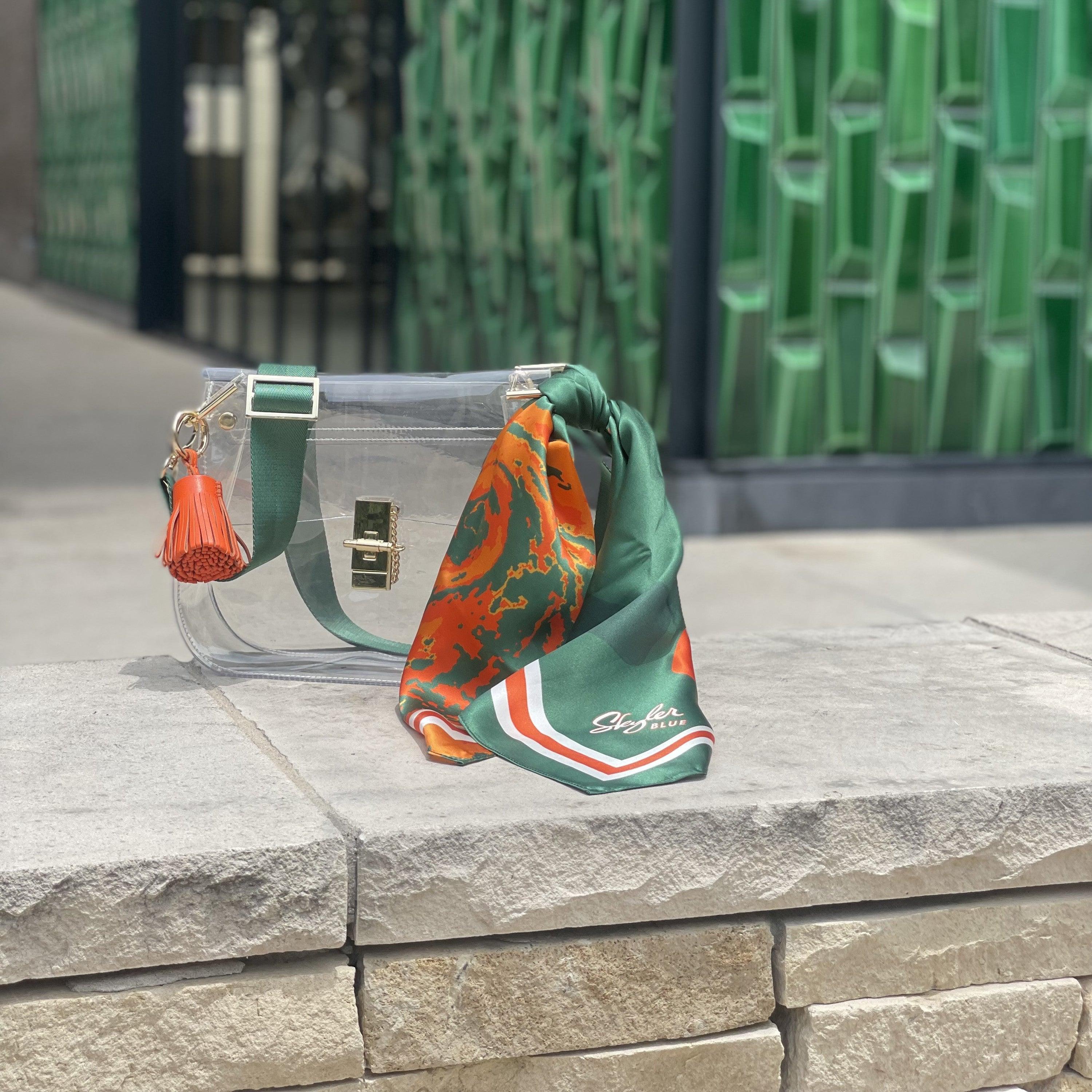 Skyler Blue’s The Coral Gables Medium Saddle Clear Bag stadium approved clear bag / clear purse including adjustable, nylon webbing shoulder or crossbody strap with herringbone weave and gold hardware, 60-centimeter 100% silk twill scarf, and 100% genuine leather tassel.