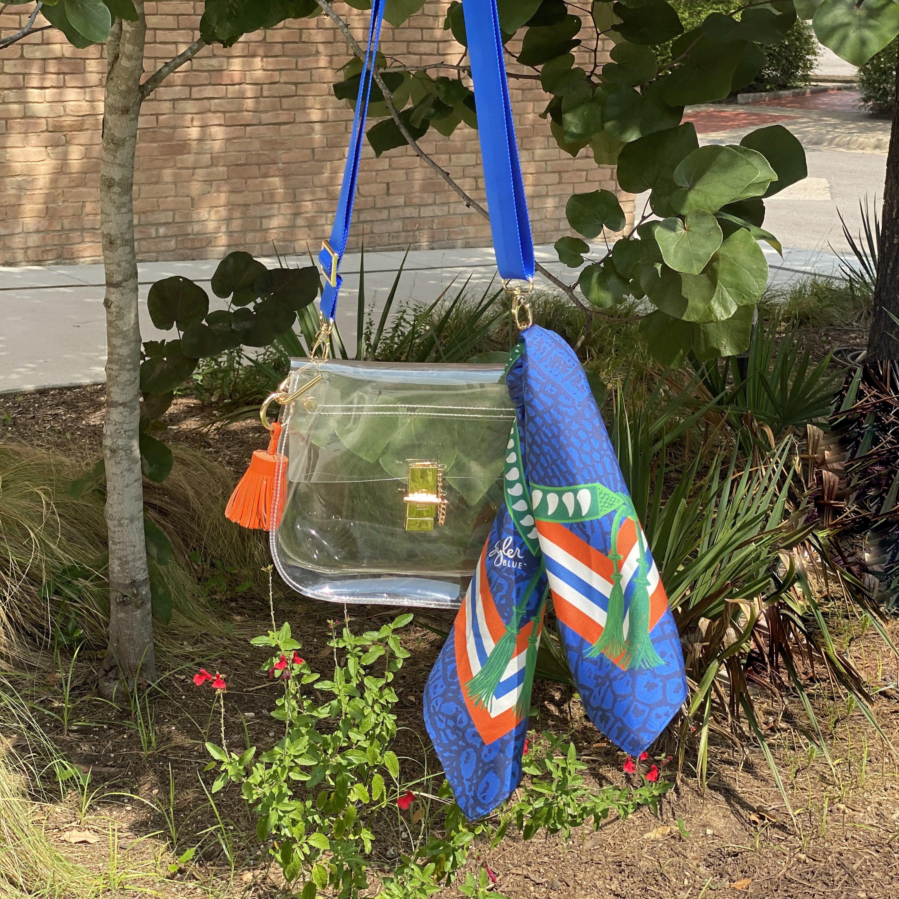 Skyler Blue’s The Gainesville Medium Saddle Clear Bag stadium approved clear bag / clear purse including adjustable, nylon webbing shoulder or crossbody strap with herringbone weave and gold hardware, 60-centimeter 100% silk twill scarf, and 100% genuine leather tassel.