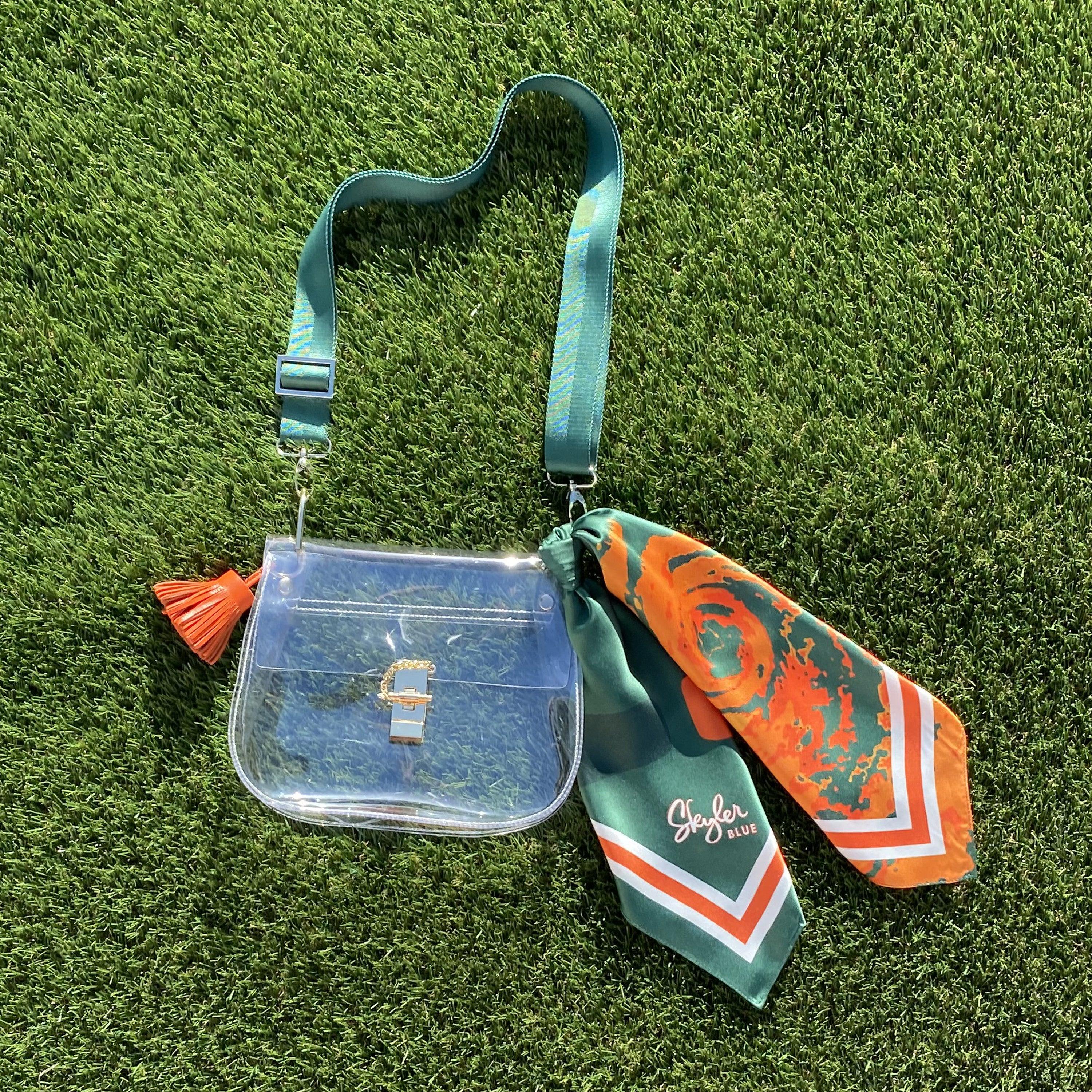 Skyler Blue’s The Coral Gables Medium Saddle Clear Bag stadium approved clear bag / clear purse including adjustable, nylon webbing shoulder or crossbody strap with herringbone weave and gold hardware, 60-centimeter 100% silk twill scarf, and 100% genuine leather tassel.