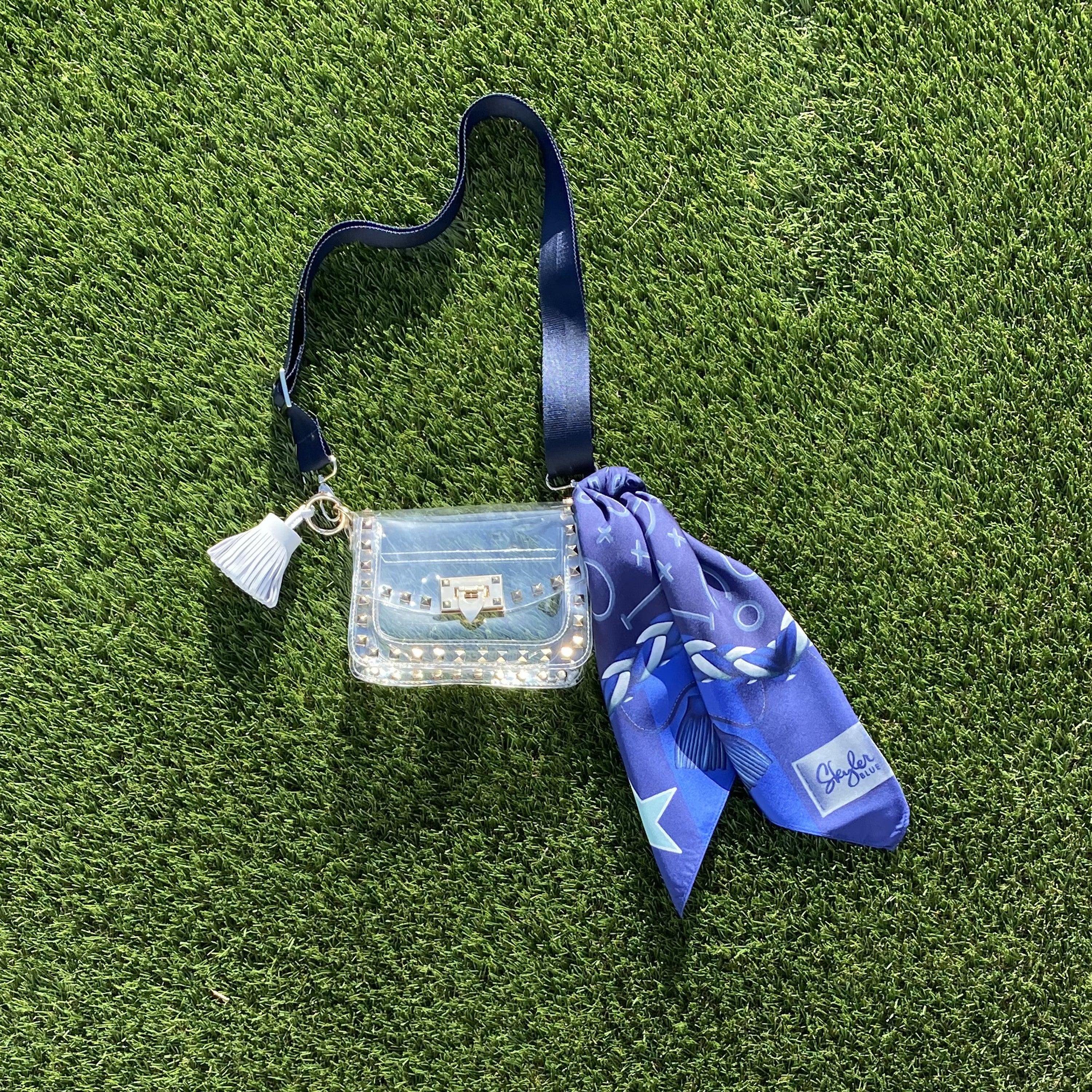 Skyler Blue’s The Dallas 001 Small Studded Clear Bag stadium approved clear bag / clear purse including adjustable, nylon webbing shoulder or crossbody strap with herringbone weave and gold hardware, 60-centimeter 100% silk twill scarf, and 100% genuine leather tassel.