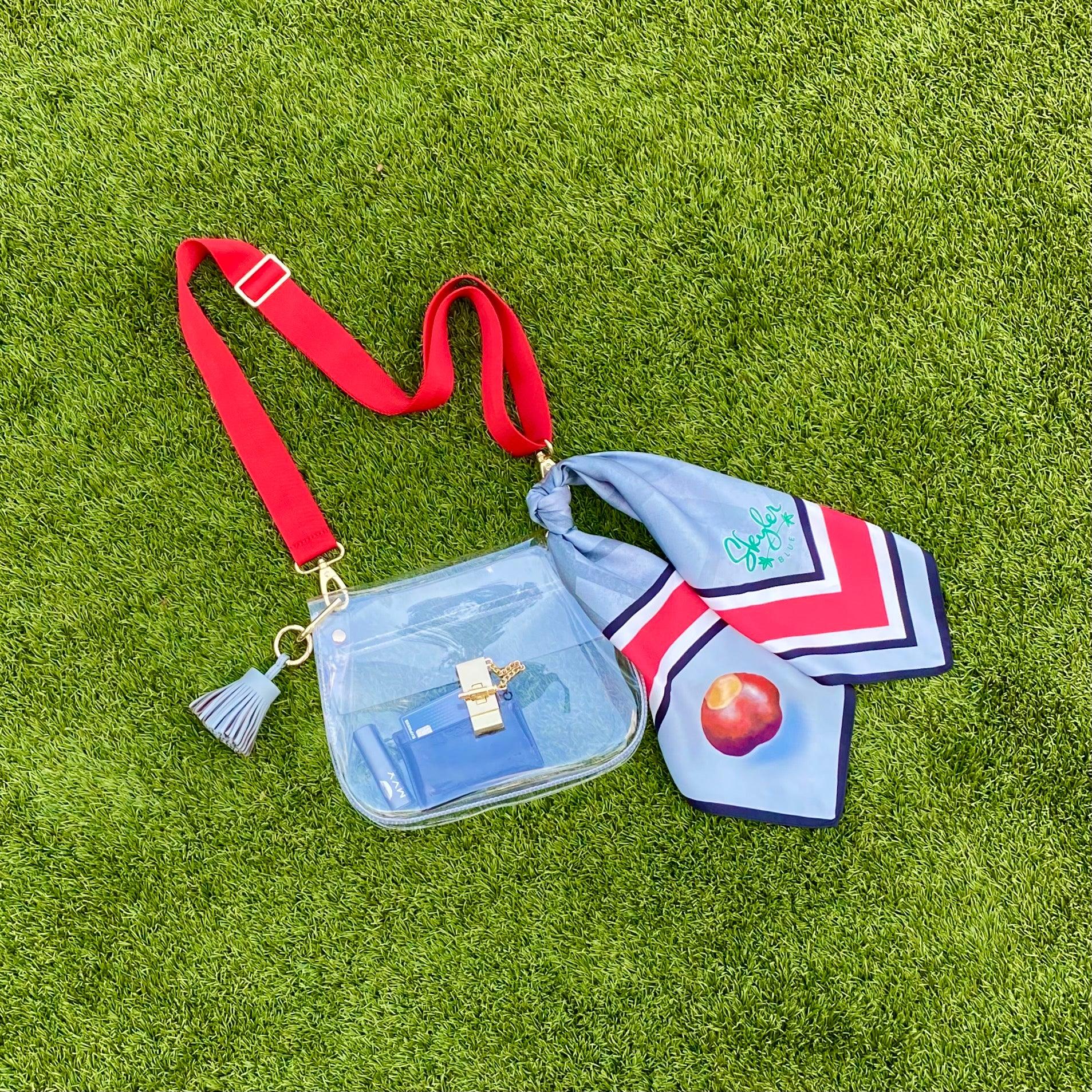Skyler Blue’s The Columbus Medium Saddle Clear Bag stadium approved clear bag / clear purse including adjustable, nylon webbing shoulder or crossbody strap with herringbone weave and gold hardware, 60-centimeter 100% silk twill scarf, and 100% genuine leather tassel.