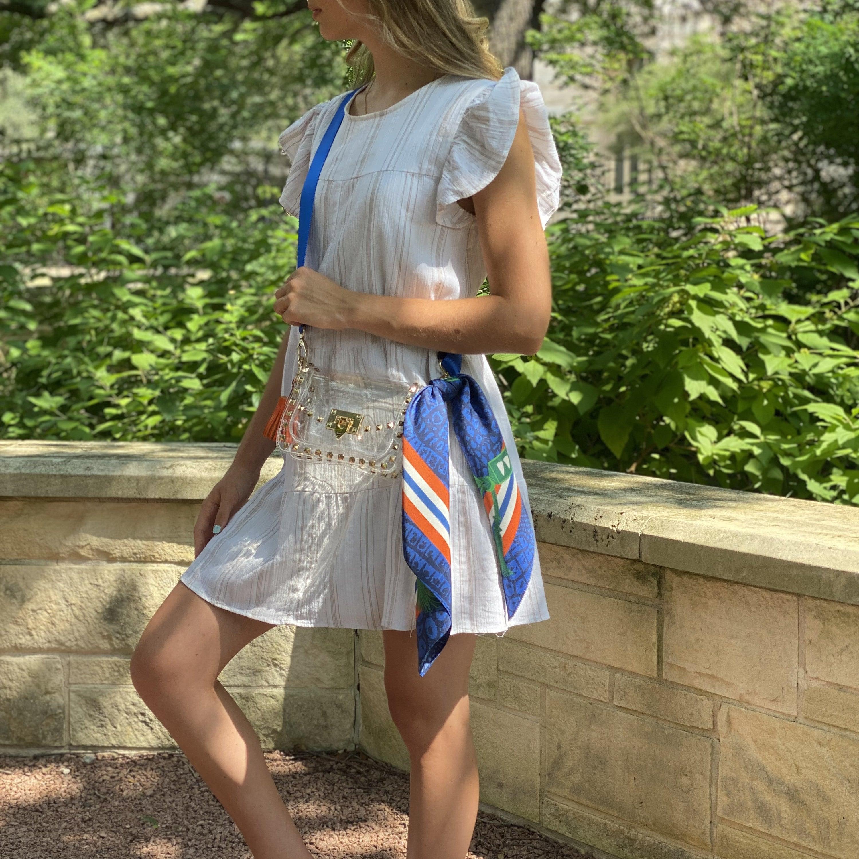 Model wearing Skyler Blue’s The Gainesville Small Studded Clear Bag stadium approved clear bag / clear purse including adjustable, nylon webbing shoulder or crossbody strap with herringbone weave and gold hardware, 60-centimeter 100% silk twill scarf, and 100% genuine leather tassel.
