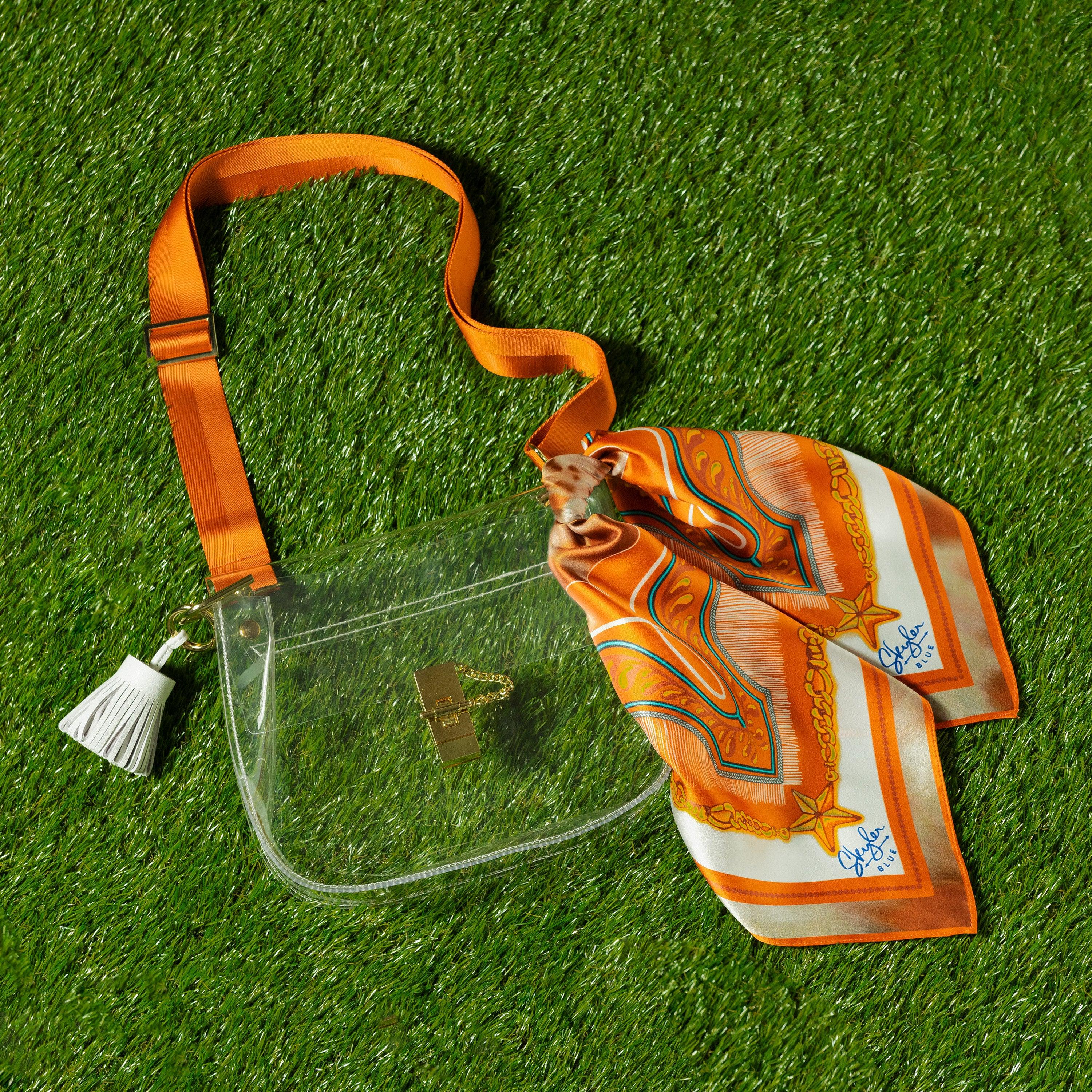 Skyler Blue’s The Austin 001 Medium Saddle Clear Bag stadium approved clear bag / clear purse including adjustable, nylon webbing shoulder or crossbody strap with herringbone weave and gold hardware, 60-centimeter 100% silk twill scarf, and 100% genuine leather tassel.