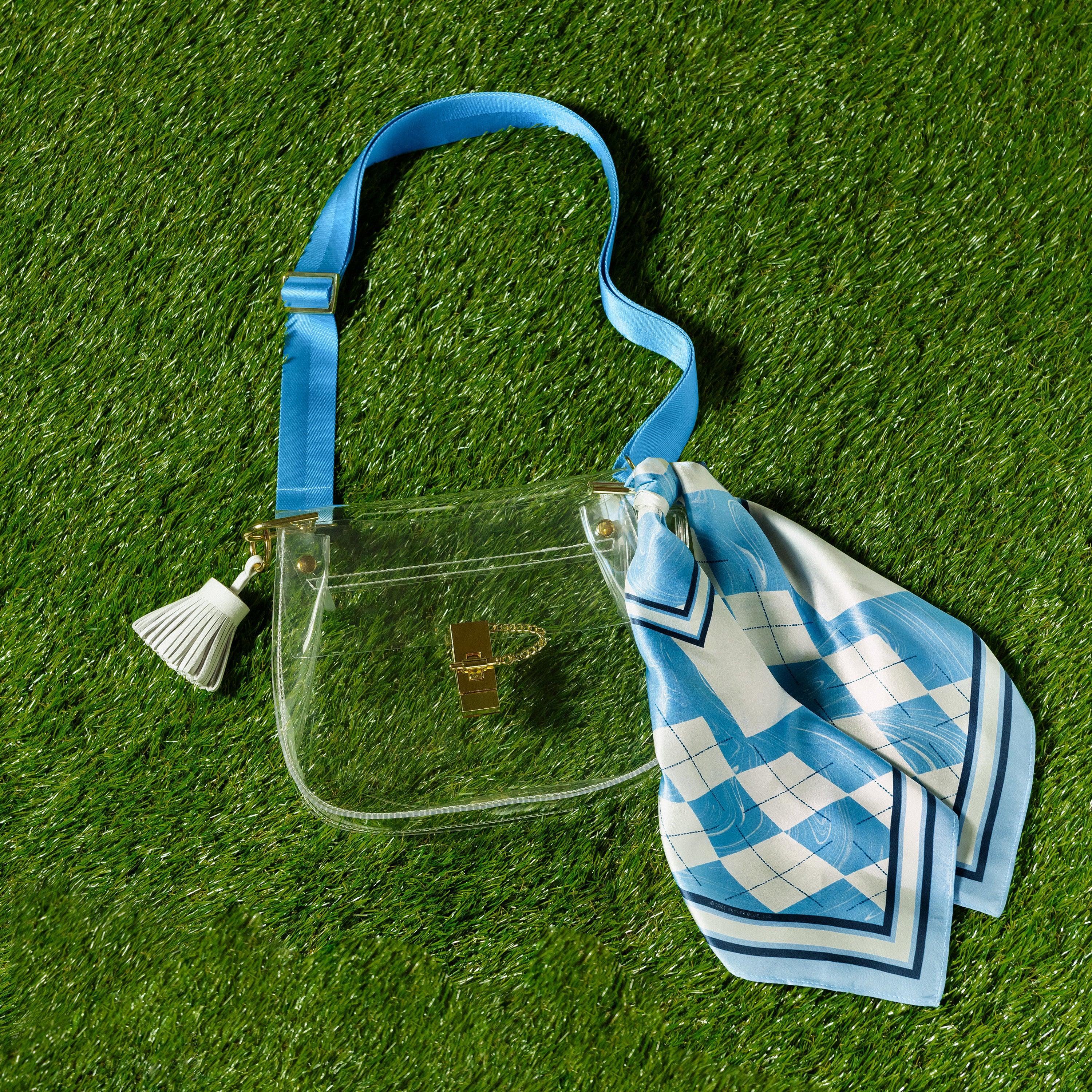 Skyler Blue’s The Chapel Hill Medium Saddle Clear Bag stadium approved clear bag / clear purse including adjustable, nylon webbing shoulder or crossbody strap with herringbone weave and gold hardware, 60-centimeter 100% silk twill scarf, and 100% genuine leather tassel.