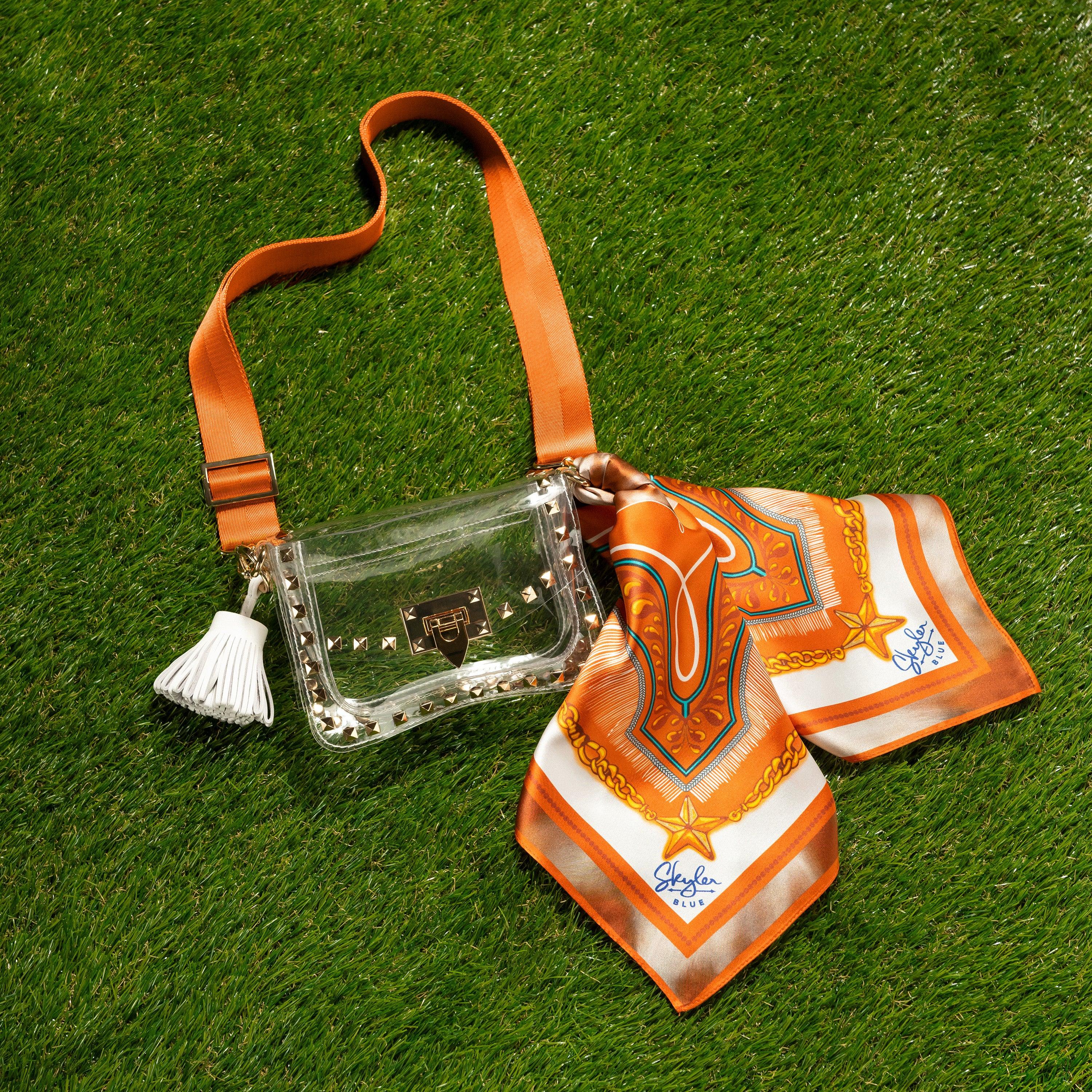 Skyler Blue’s The Austin 001 Small Studded Clear Bag stadium approved clear bag / clear purse including adjustable, nylon webbing shoulder or crossbody strap with herringbone weave and gold hardware, 60-centimeter 100% silk twill scarf, and 100% genuine leather tassel.