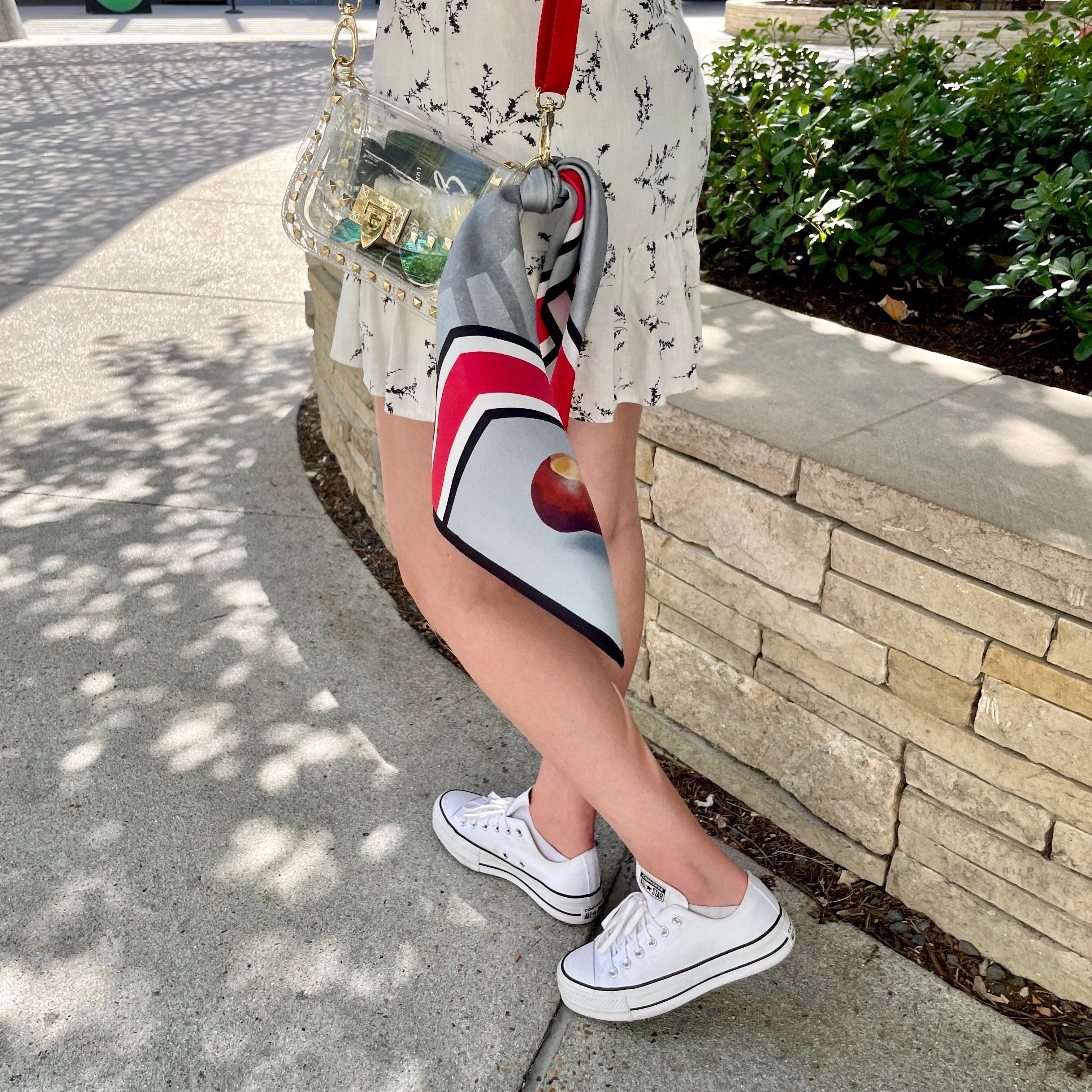 Model wearing Skyler Blue’s The Columbus Small Studded Clear Bag stadium approved clear bag / clear purse including adjustable, nylon webbing shoulder or crossbody strap with herringbone weave and gold hardware, 60-centimeter 100% silk twill scarf, and 100% genuine leather tassel.
