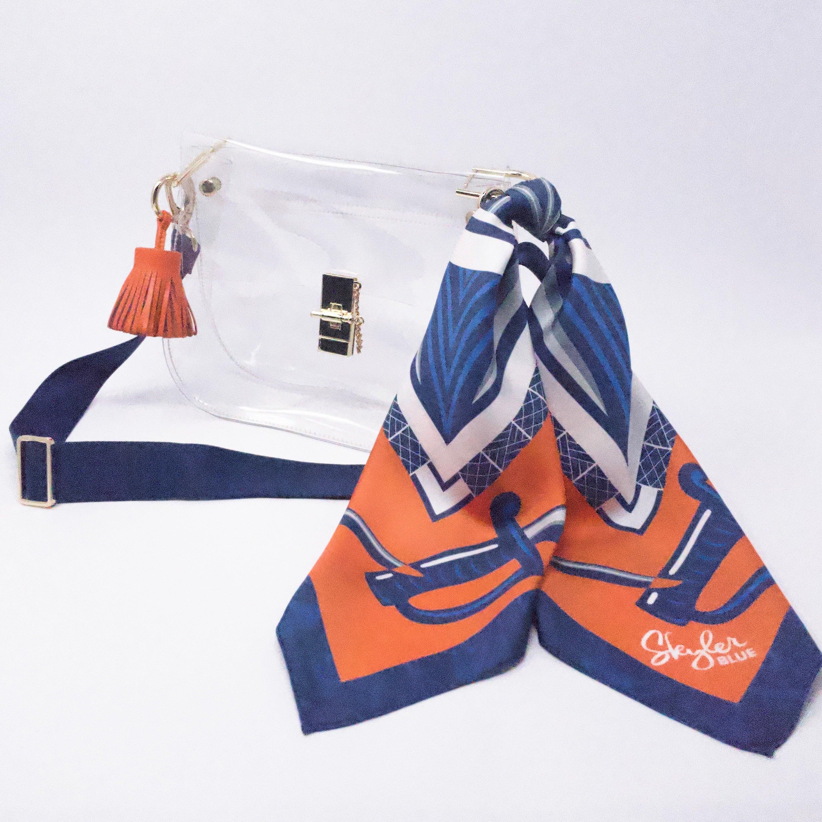 Skyler Blue’s The Charlottesville Medium Saddle Clear Bag stadium approved clear bag / clear purse including adjustable, nylon webbing shoulder or crossbody strap with herringbone weave and gold hardware, 60-centimeter 100% silk twill scarf, and 100% genuine leather tassel.
