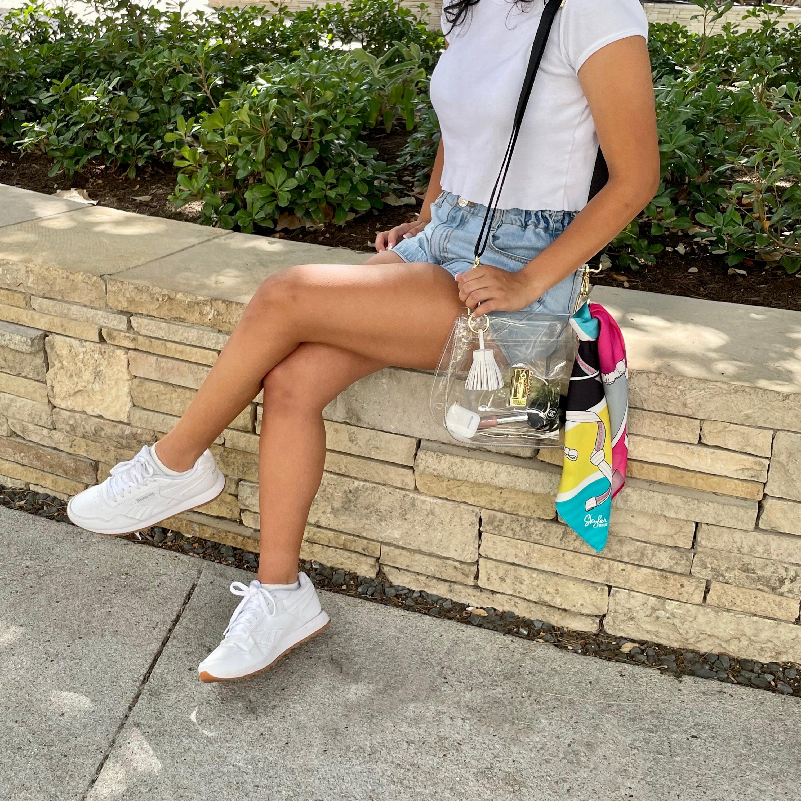 Model wearing Skyler Blue’s The Bikini Medium Saddle Clear Bag stadium approved clear bag / clear purse including adjustable, nylon webbing shoulder or crossbody strap with herringbone weave and gold hardware, 60-centimeter 100% silk twill scarf, and 100% genuine leather tassel.