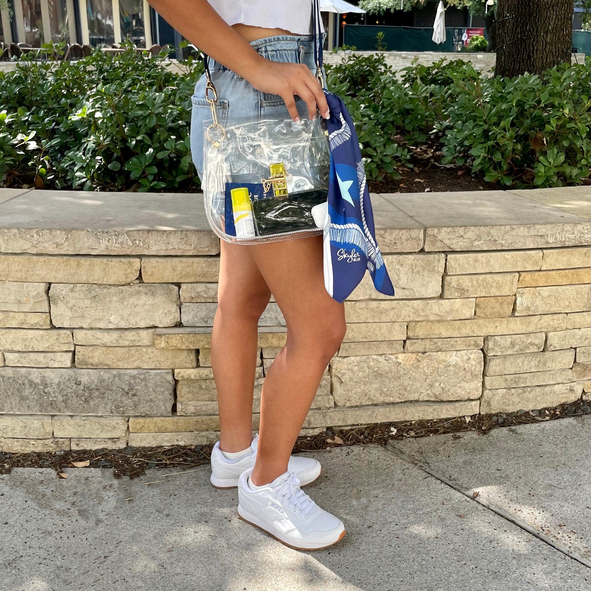 Model wearing Skyler Blue’s The Dallas 002 Medium Saddle Clear Bag stadium approved clear bag / clear purse including adjustable, nylon webbing shoulder or crossbody strap with herringbone weave and gold hardware, 60-centimeter 100% silk twill scarf, and 100% genuine leather tassel.