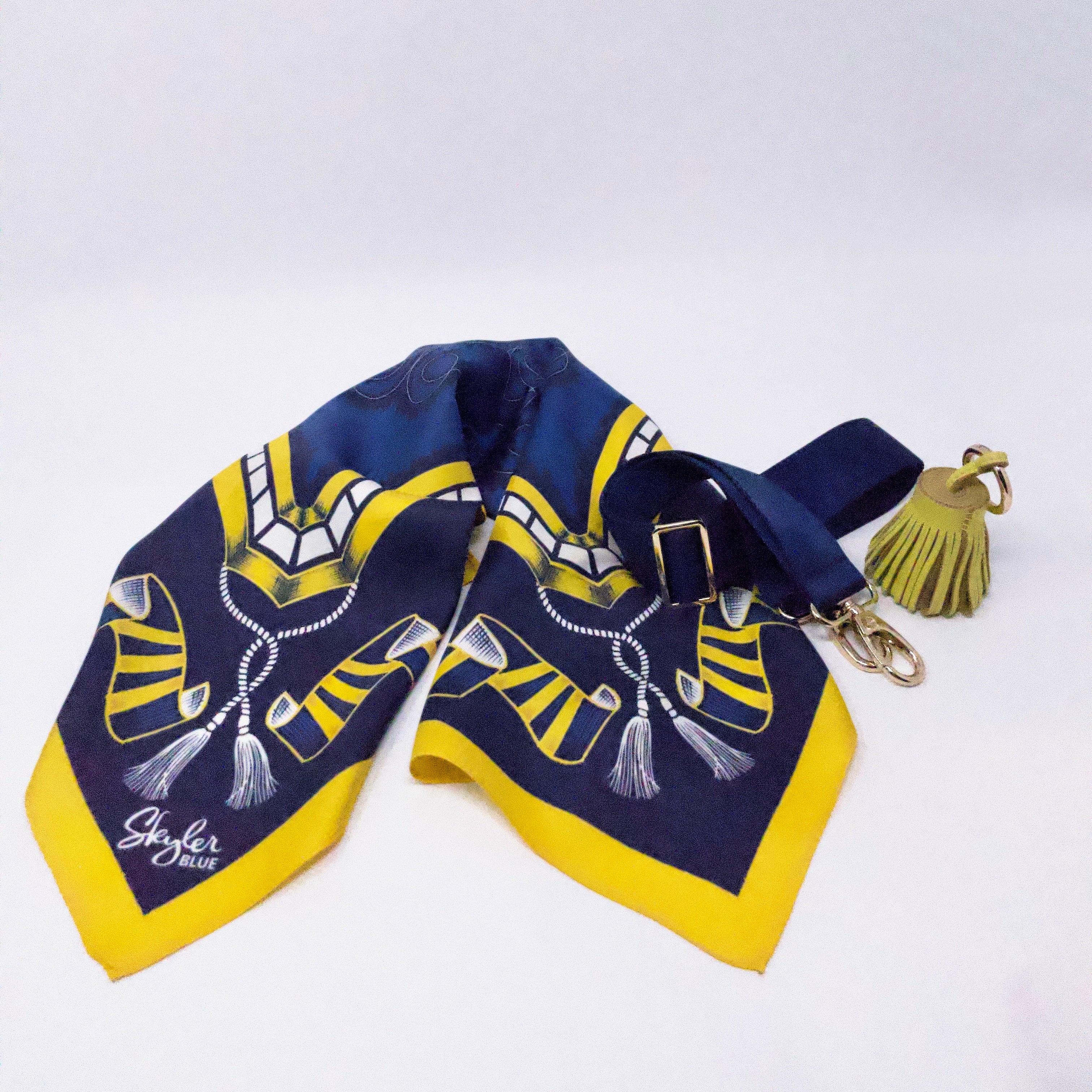 Skyler Blue’s The Ann Arbor Accessory Package including adjustable, nylon webbing shoulder or crossbody strap with herringbone weave and gold hardware, 60-centimeter 100% silk twill scarf, and 100% genuine leather tassel. 