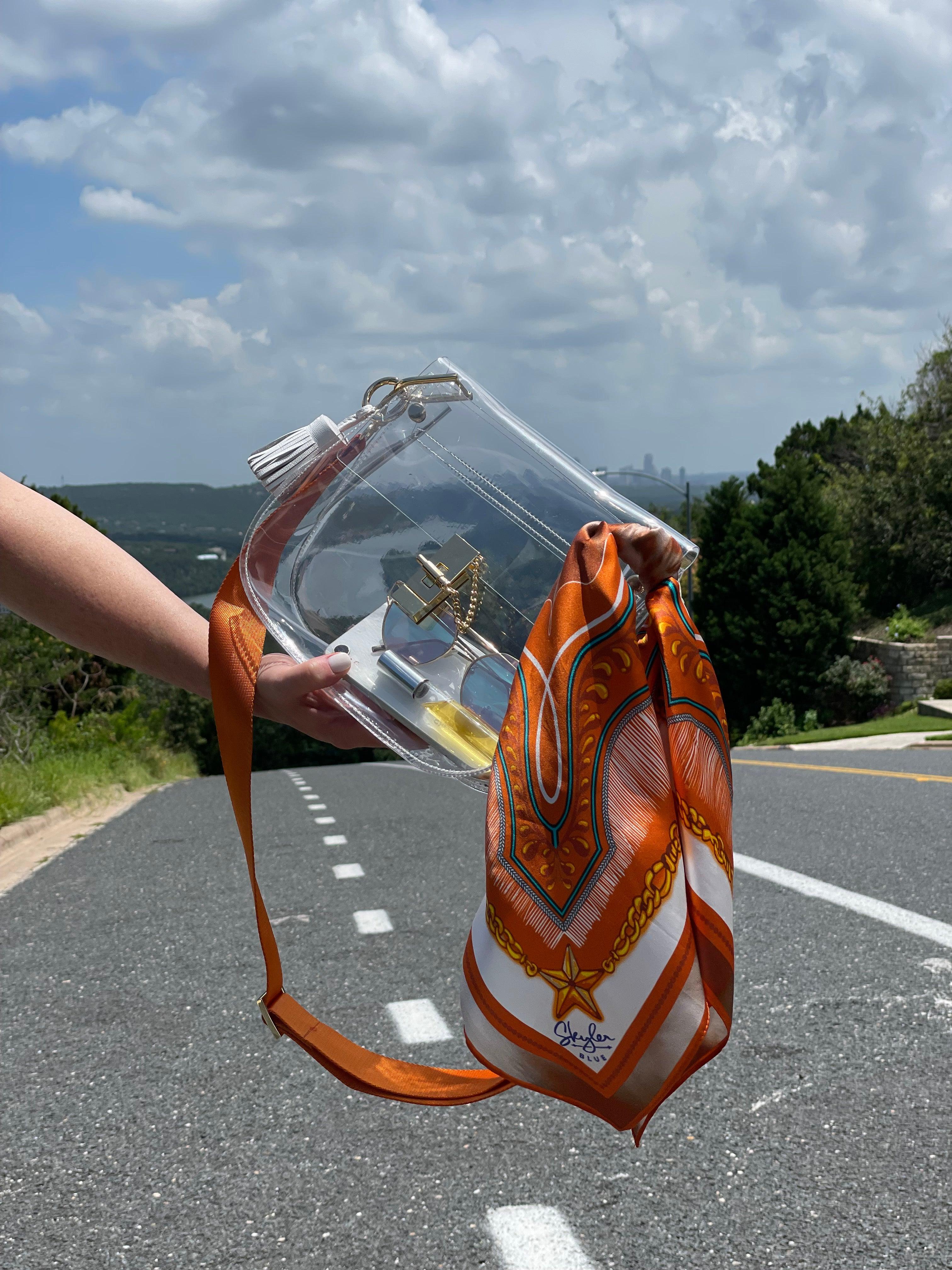 Skyler Blue’s The Austin 001 Medium Saddle Clear Bag stadium approved clear bag / clear purse including adjustable, nylon webbing shoulder or crossbody strap with herringbone weave and gold hardware, 60-centimeter 100% silk twill scarf, and 100% genuine leather tassel. 