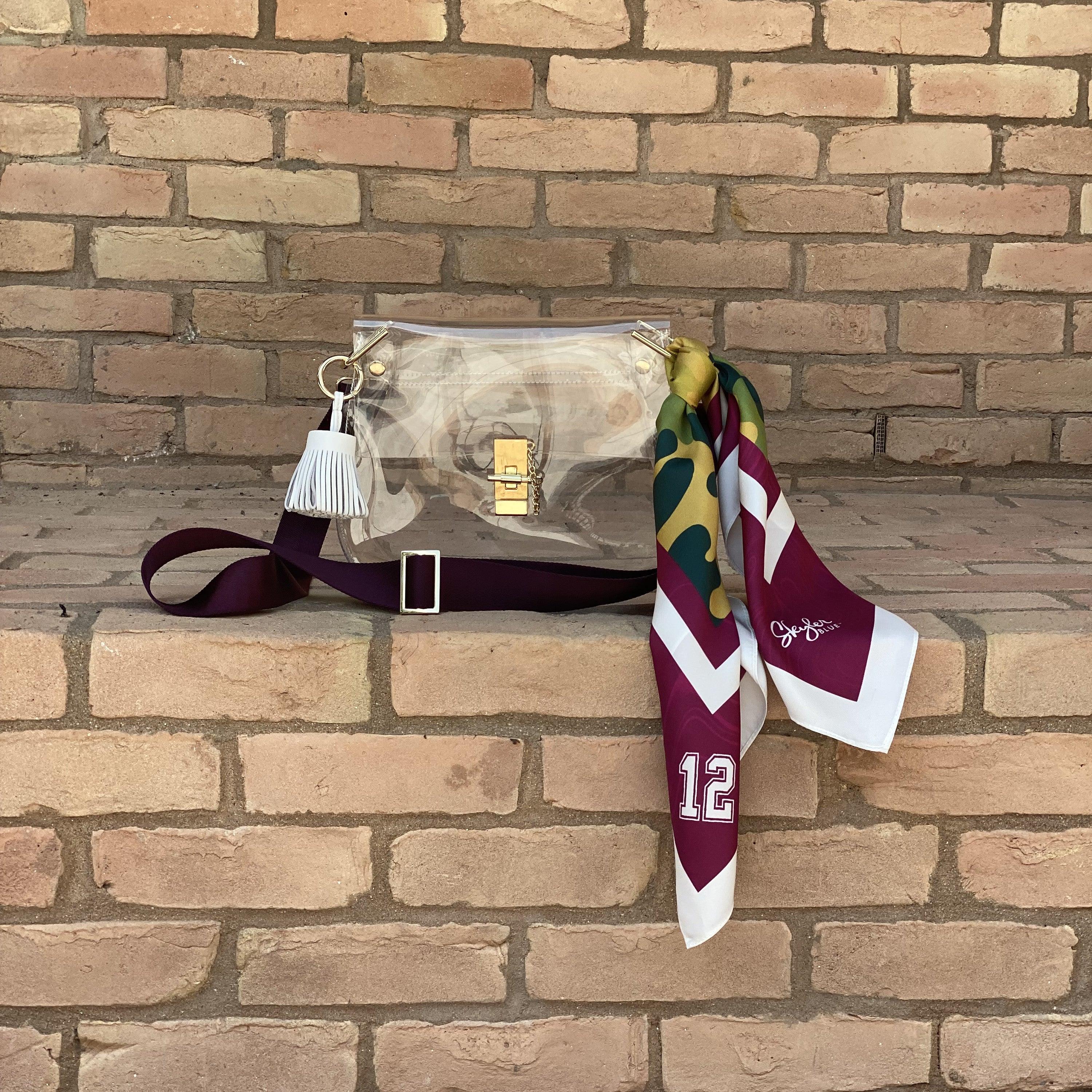 Skyler Blue’s The College Station Medium Saddle Clear Bag stadium approved clear bag / clear purse including adjustable, nylon webbing shoulder or crossbody strap with herringbone weave and gold hardware, 60-centimeter 100% silk twill scarf, and 100% genuine leather tassel. 