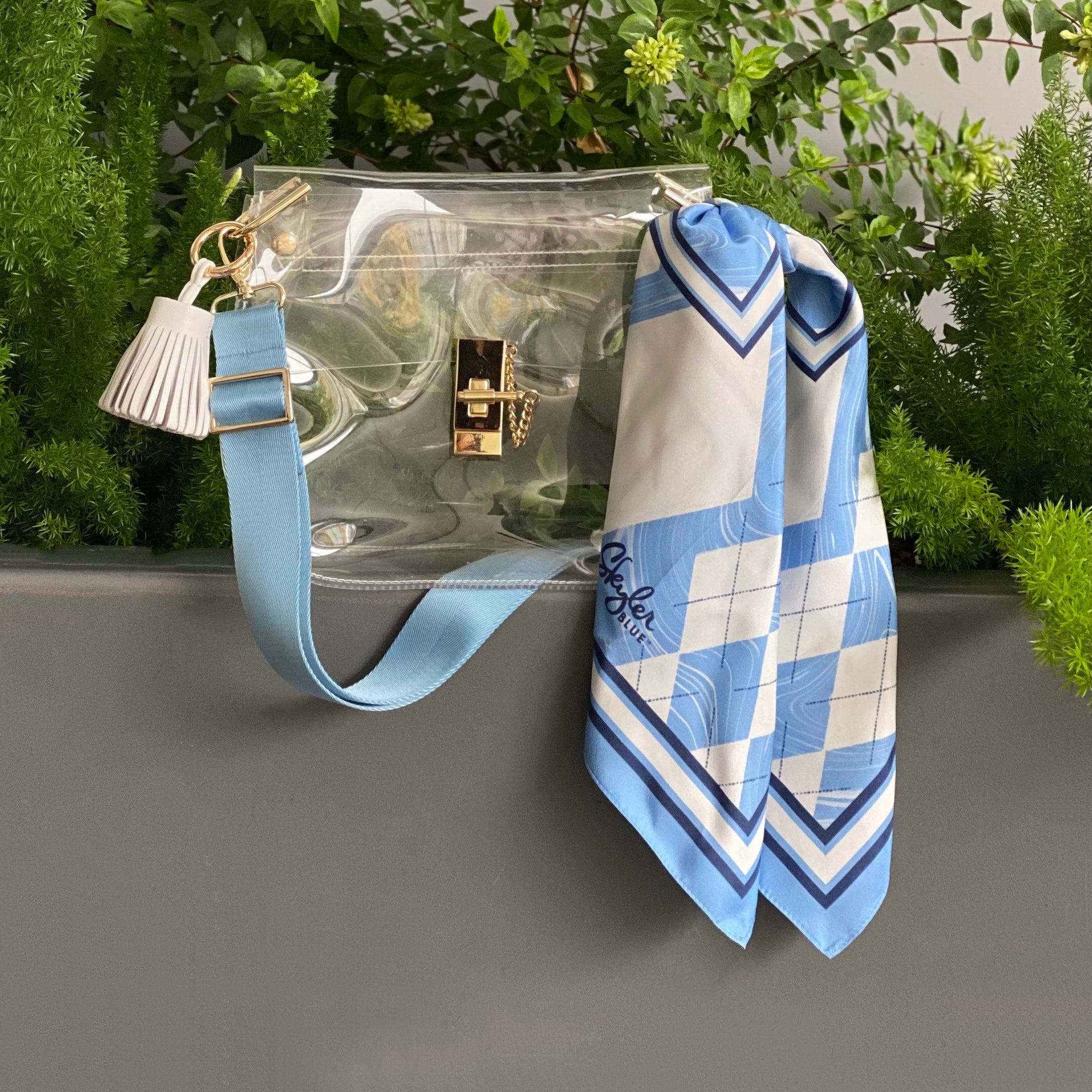 Skyler Blue’s The Chapel Hill Medium Saddle Clear Bag stadium approved clear bag / clear purse including adjustable, nylon webbing shoulder or crossbody strap with herringbone weave and gold hardware, 60-centimeter 100% silk twill scarf, and 100% genuine leather tassel. 