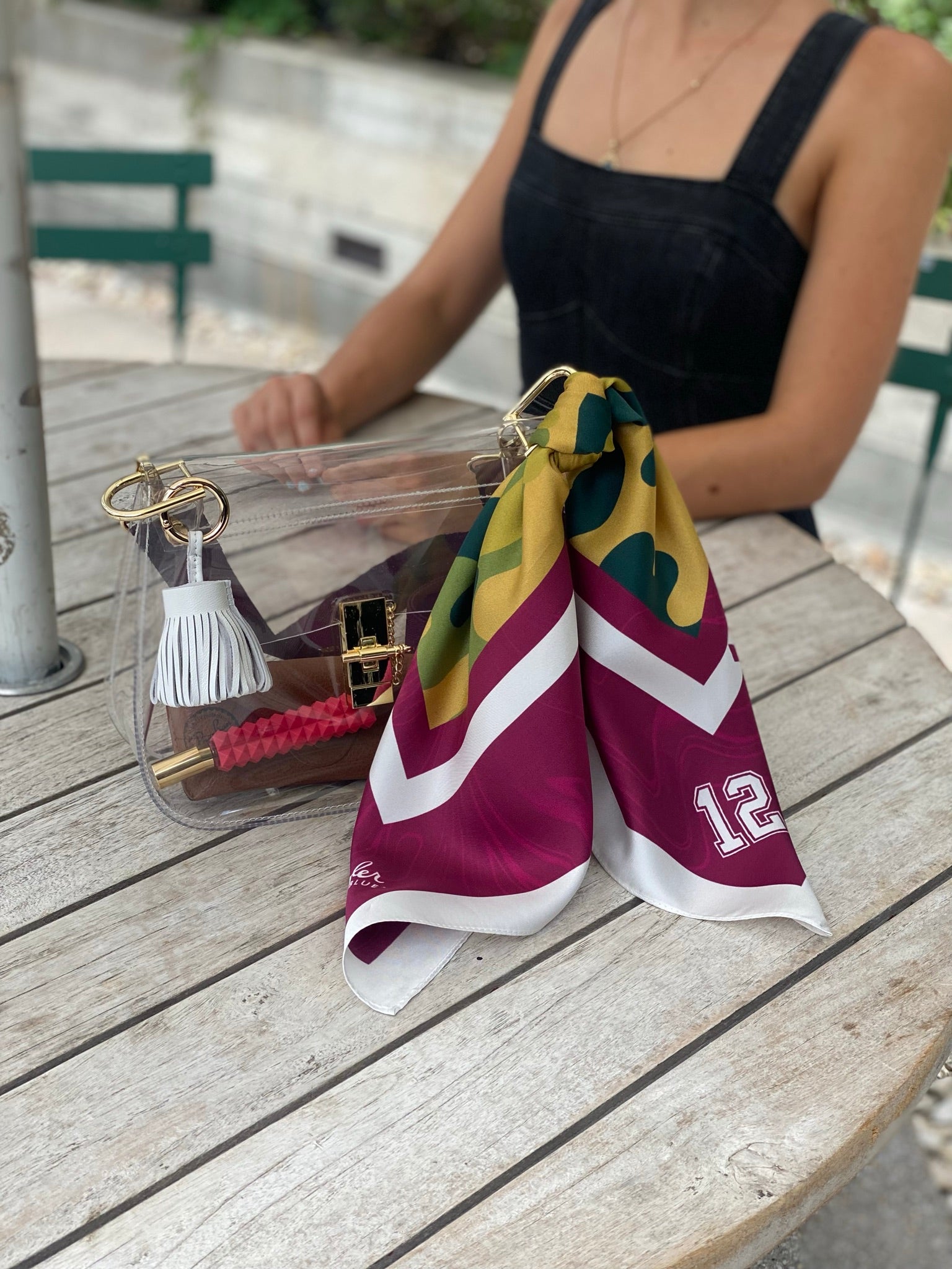 Model with Skyler Blue’s The College Station Medium Saddle Clear Bag stadium approved clear bag / clear purse including adjustable, nylon webbing shoulder or crossbody strap with herringbone weave and gold hardware, 60-centimeter 100% silk twill scarf, and 100% genuine leather tassel. 