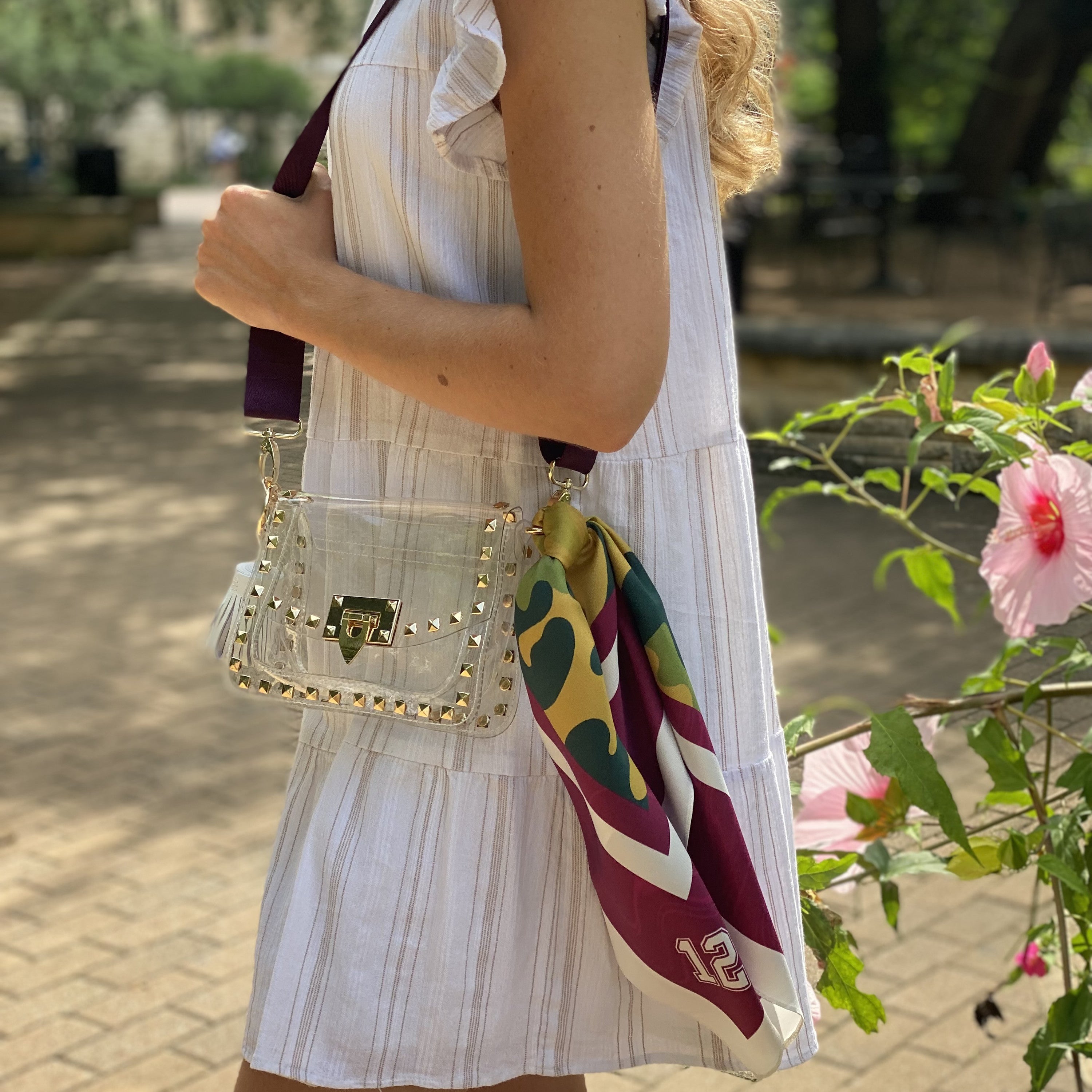 Model wearing Skyler Blue’s The College Station Small Studded Clear Bag stadium approved clear bag / clear purse including adjustable, nylon webbing shoulder or crossbody strap with herringbone weave and gold hardware, 60-centimeter 100% silk twill scarf, and 100% genuine leather tassel. 