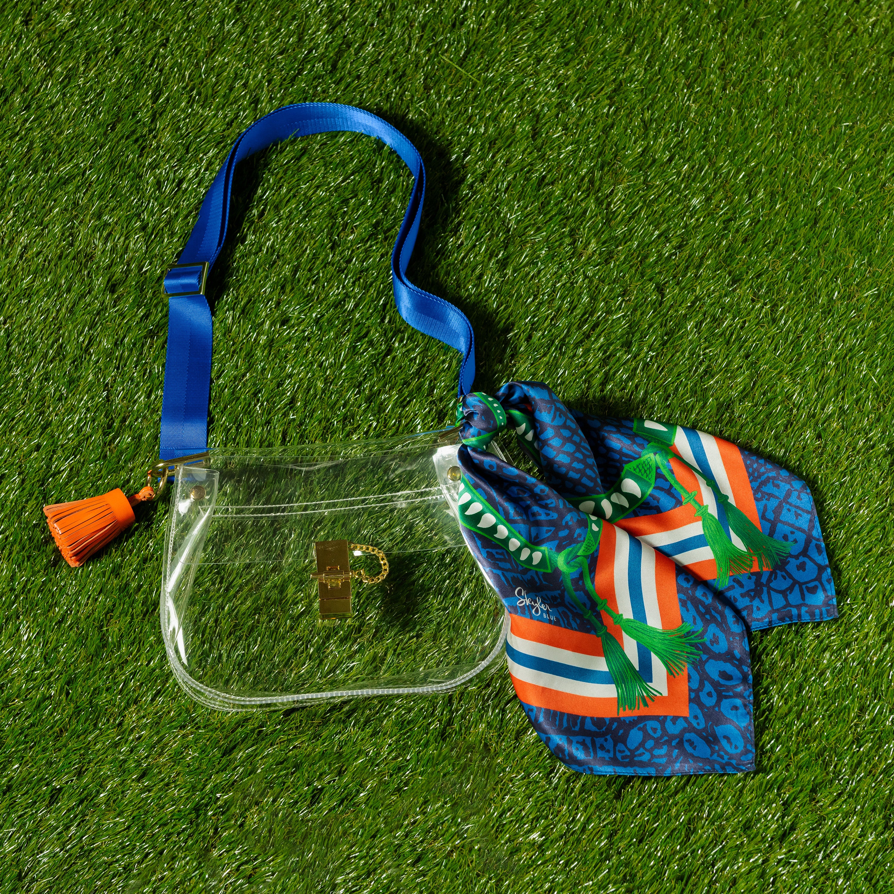 Skyler Blue’s The Gainesville Medium Saddle Clear Bag stadium approved clear bag / clear purse including adjustable, nylon webbing shoulder or crossbody strap with herringbone weave and gold hardware, 60-centimeter 100% silk twill scarf, and 100% genuine leather tassel. 