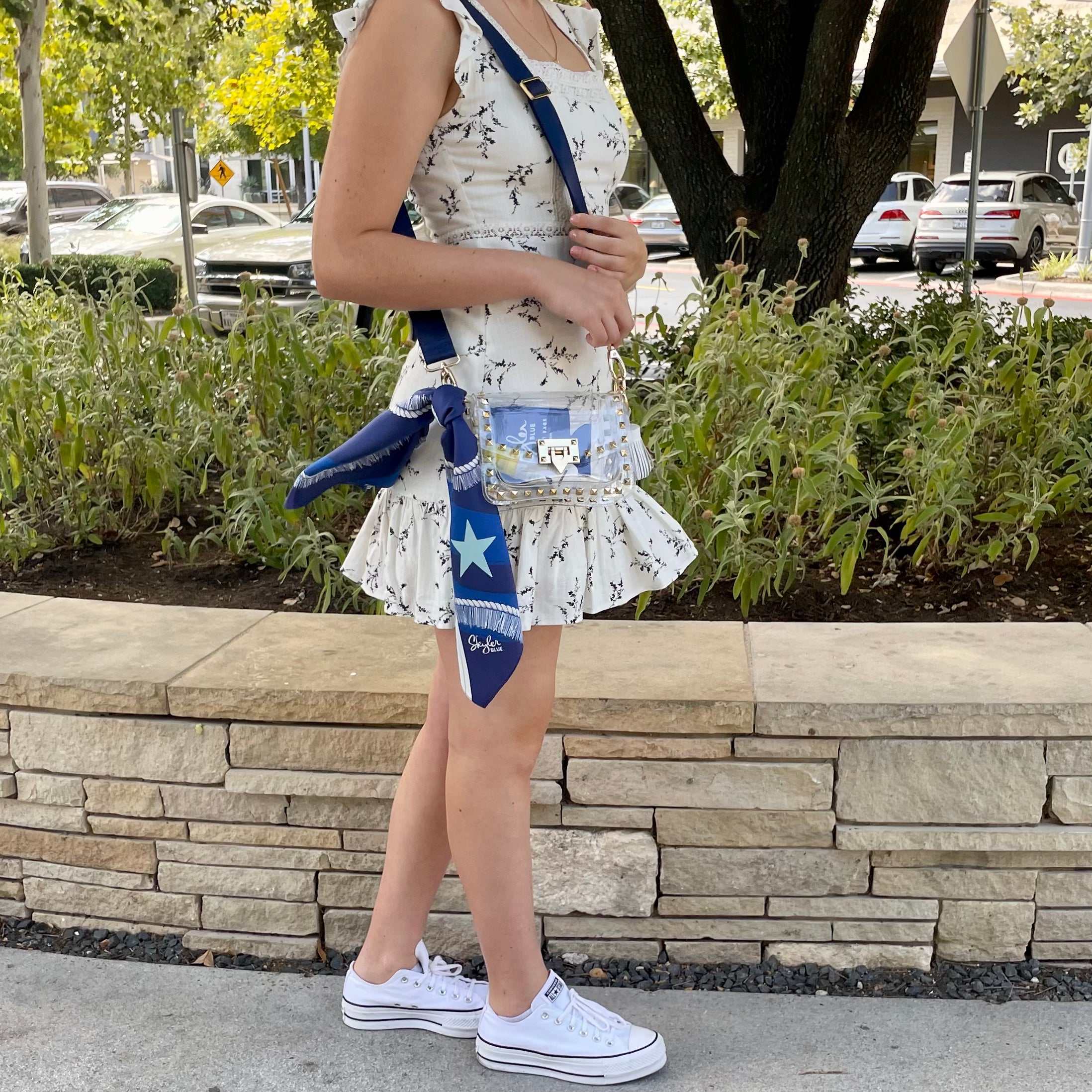 Model wearing Skyler Blue’s The Dallas 002 Small Studded Clear Bag stadium approved clear bag / clear purse including adjustable, nylon webbing shoulder or crossbody strap with herringbone weave and gold hardware, 60-centimeter 100% silk twill scarf, and 100% genuine leather tassel. 