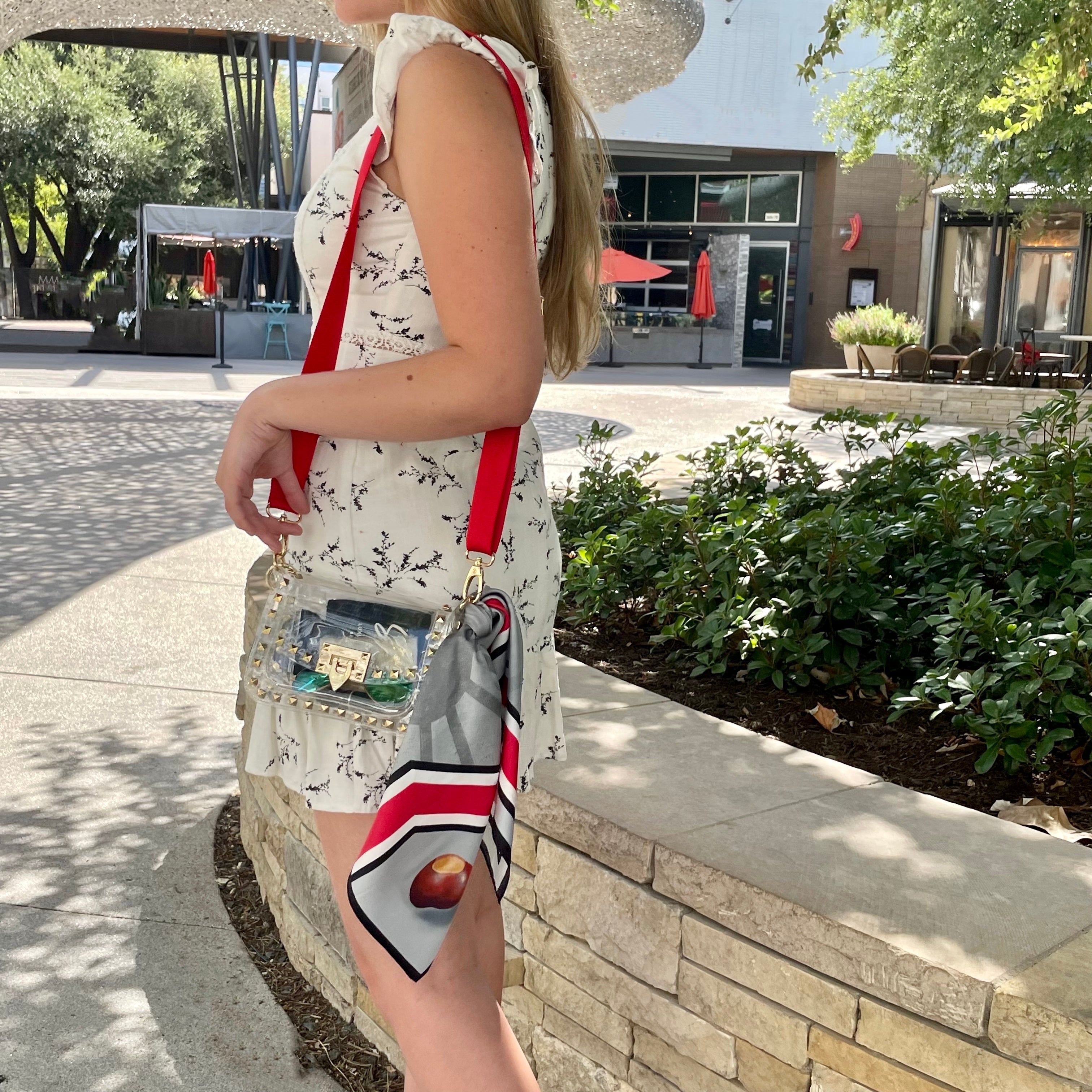 Model wearing Skyler Blue’s The Columbus Small Studded Clear Bag stadium approved clear bag / clear purse including adjustable, nylon webbing shoulder or crossbody strap with herringbone weave and gold hardware, 60-centimeter 100% silk twill scarf, and 100% genuine leather tassel. 