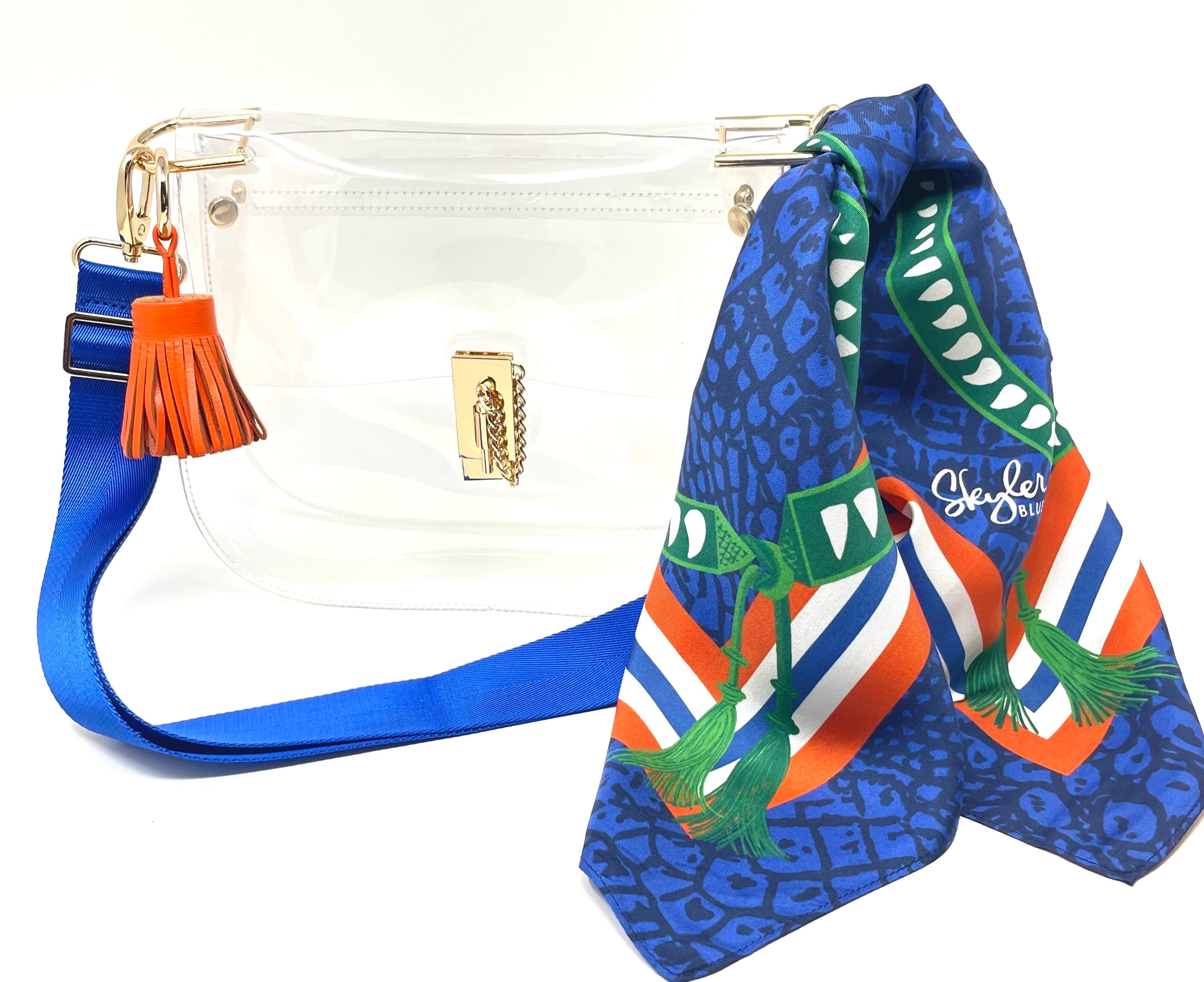 Skyler Blue’s The Gainesville Medium Saddle Clear Bag stadium approved clear bag / clear purse including adjustable, nylon webbing shoulder or crossbody strap with herringbone weave and gold hardware, 60-centimeter 100% silk twill scarf, and 100% genuine leather tassel. 