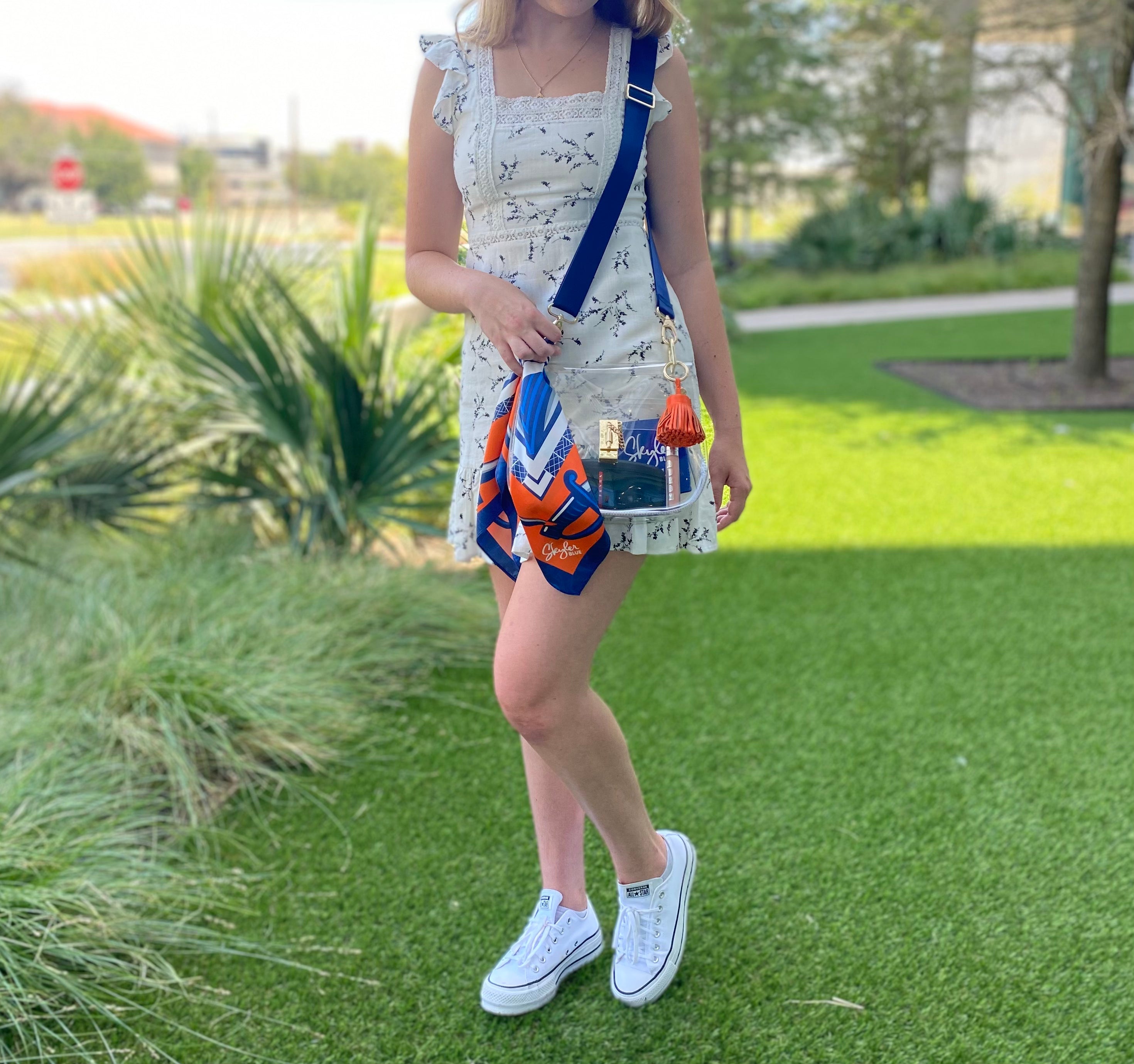 Model wearing Skyler Blue’s The Charlottesville Medium Saddle Clear Bag stadium approved clear bag / clear purse including adjustable, nylon webbing shoulder or crossbody strap with herringbone weave and gold hardware, 60-centimeter 100% silk twill scarf, and 100% genuine leather tassel. 