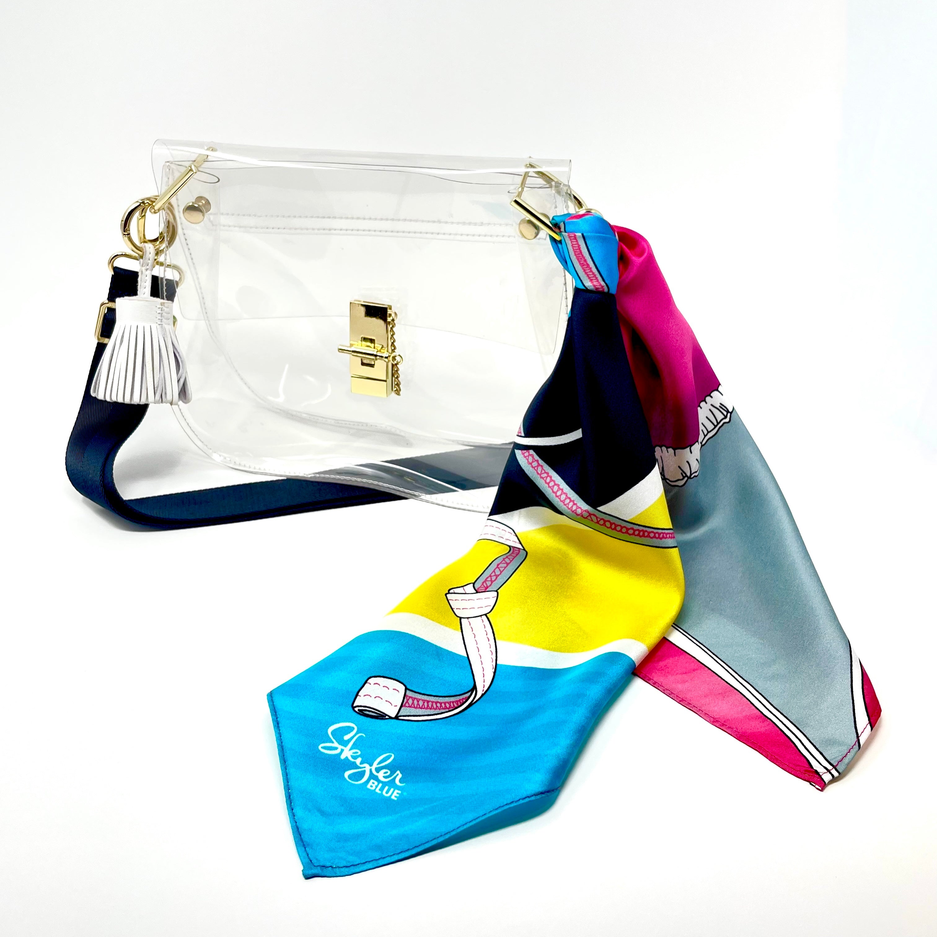 Skyler Blue’s The Bikini Medium Saddle Clear Bag stadium approved clear bag / clear purse including adjustable, nylon webbing shoulder or crossbody strap with herringbone weave and gold hardware, 60-centimeter 100% silk twill scarf, and 100% genuine leather tassel. 