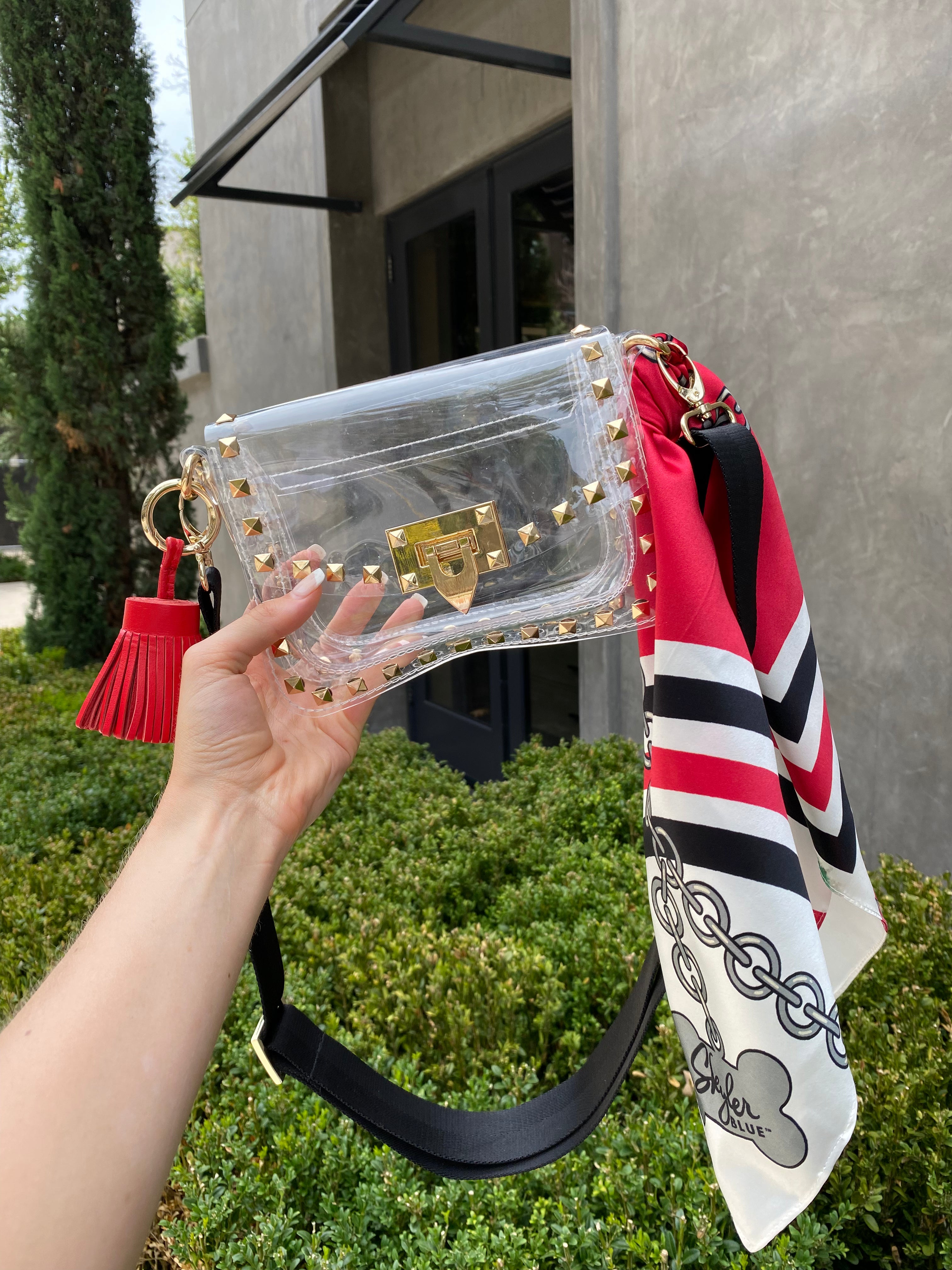 Skyler Blue’s The Athens 001 Small Studded Clear Bag stadium approved clear bag / clear purse including adjustable, nylon webbing shoulder or crossbody strap with herringbone weave and gold hardware, 60-centimeter 100% silk twill scarf, and 100% genuine leather tassel. 